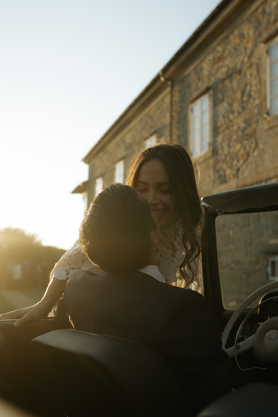 Bride and groom smiling while holding a dog dressed in a blue outfit with a smiley face collar at an indoor wedding venue.