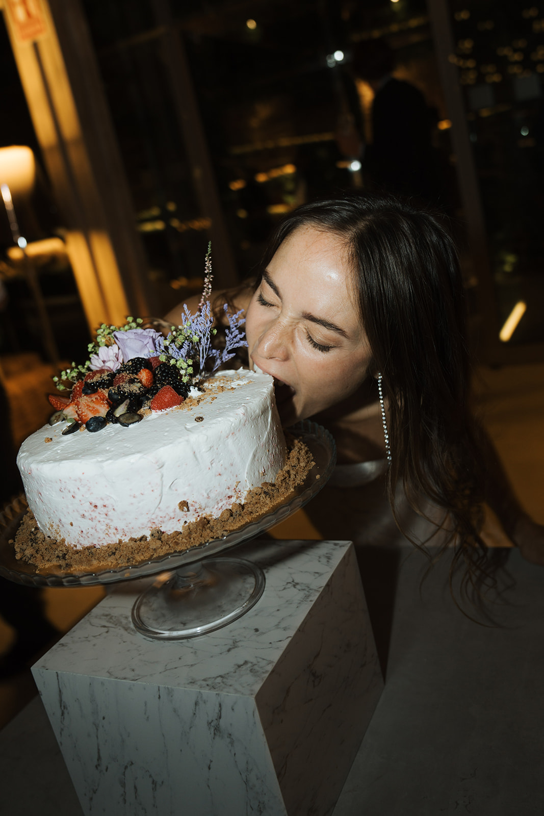 Bride in white wedding dress holding bouquet and groom in black tuxedo lying on a patterned staircase, holding hands and looking at each other.