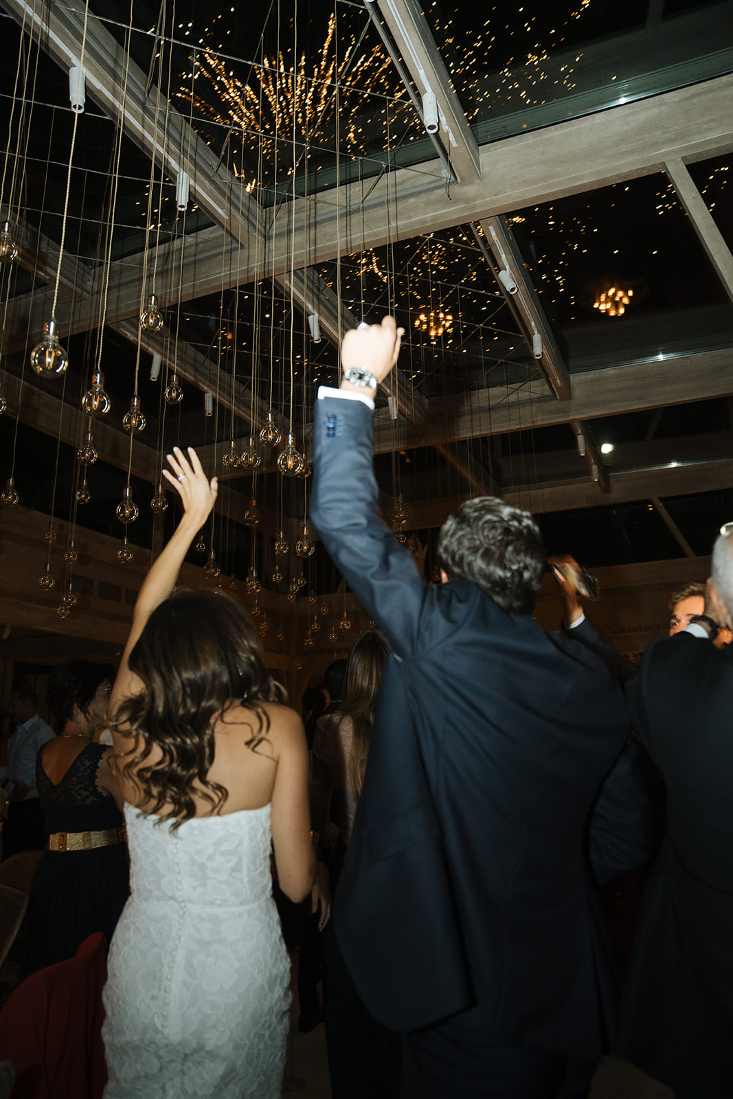 Three women in elegant dresses inside a decorated room with a chandelier, viewed through partially open doors.