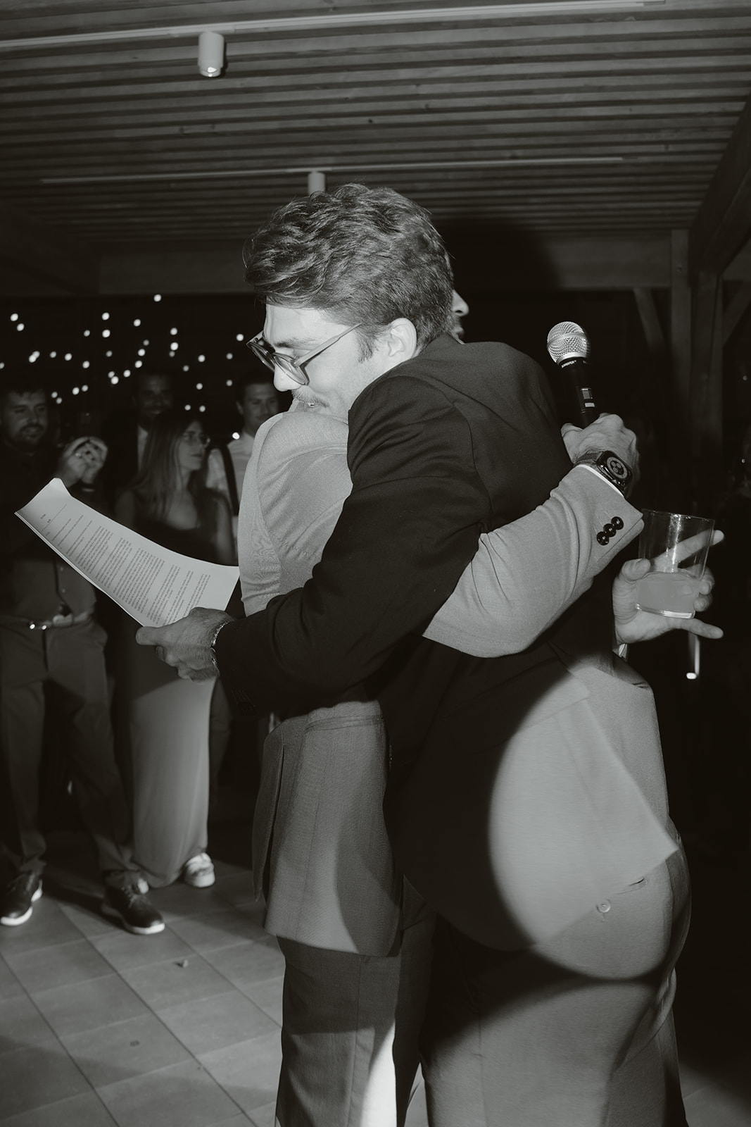 Person with manicured nails wearing gold rings resting hands on a white marble table, dressed in a white buttoned shirt.