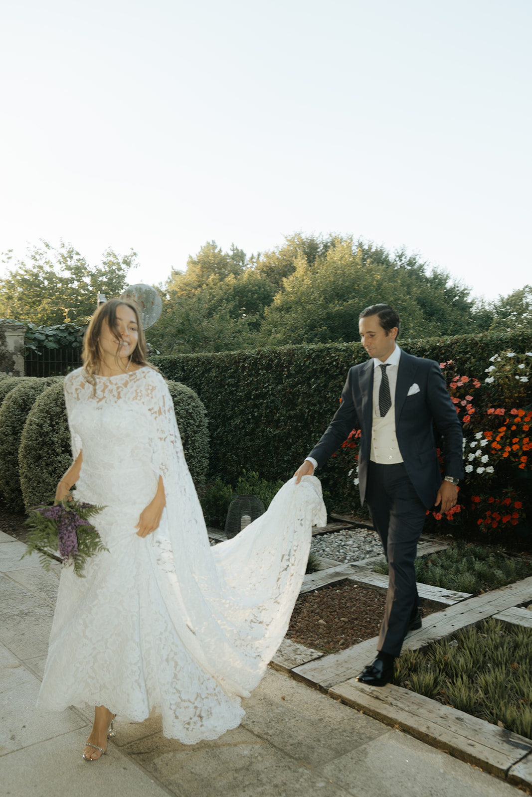 Black and white photo of a wedding party with bride and groom in the center, surrounded by bridesmaids and groomsmen on stone steps in front of an arched doorway.
