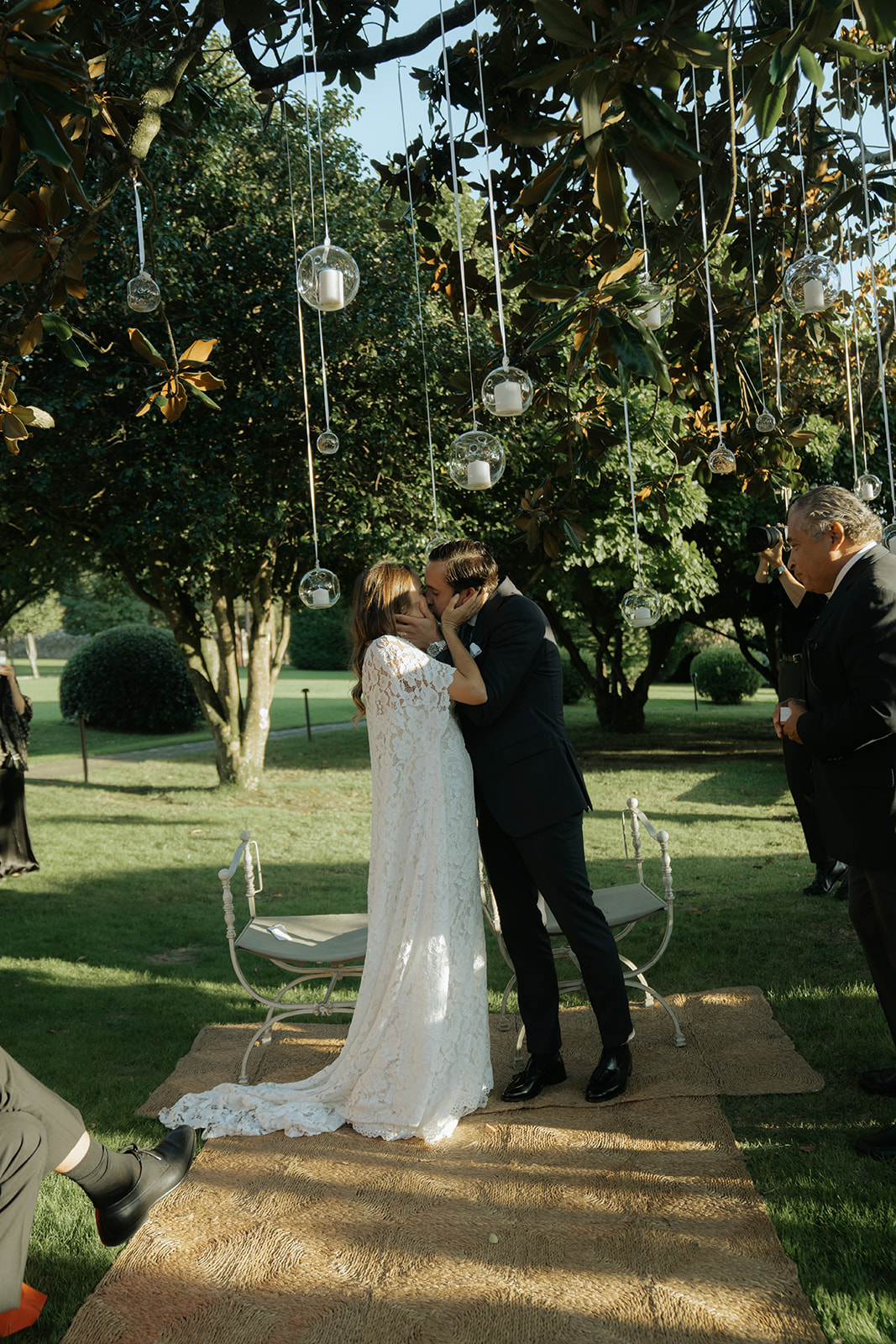Bride and groom kissing on steps with bride holding bouquet as guests throw confetti and take photos.