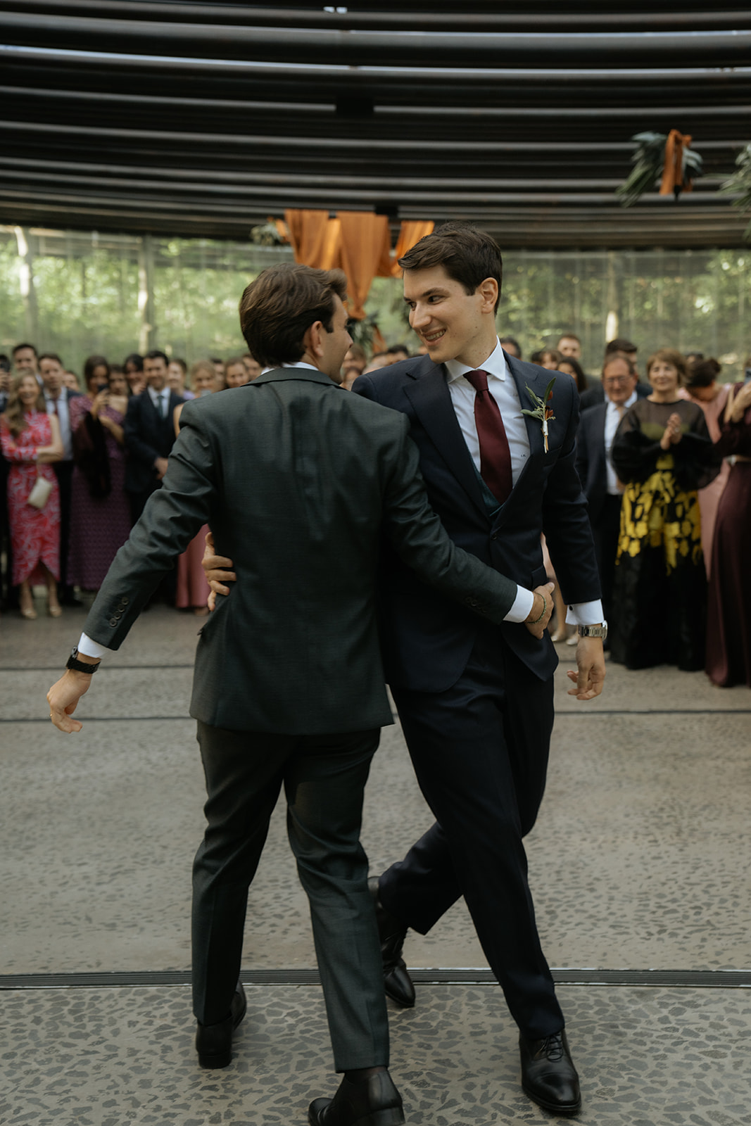 Person with manicured nails wearing gold rings resting hands on a white marble table, dressed in a white buttoned shirt.