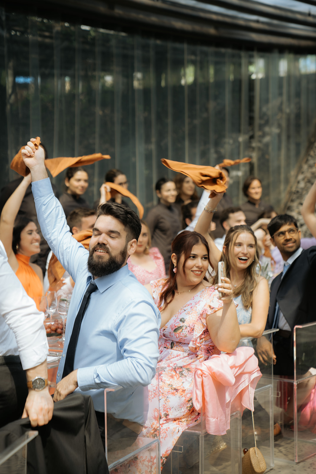 Bride and groom standing under spotlight in a grand hall surrounded by guests taking photos.