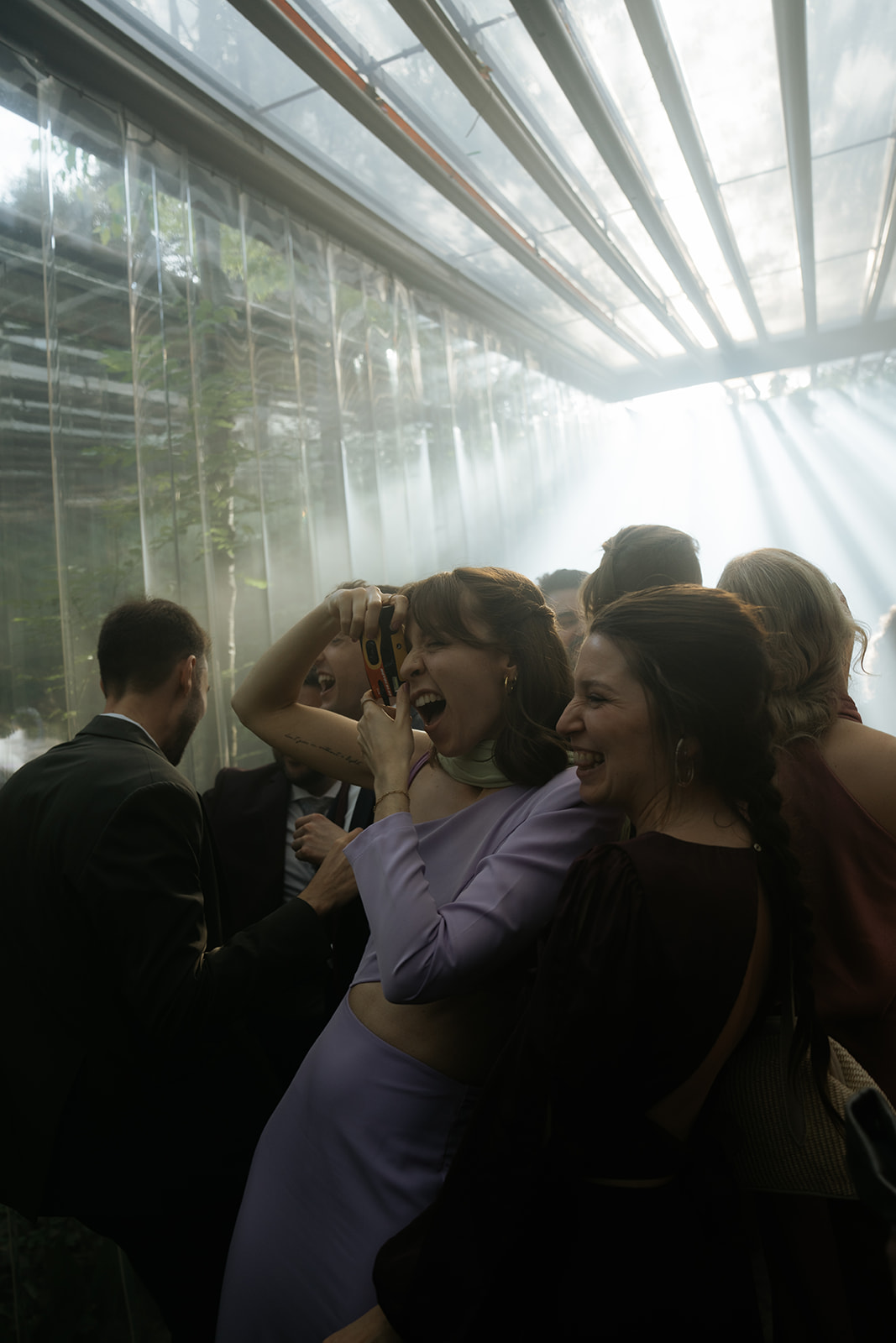 Three women in elegant dresses inside a decorated room with a chandelier, viewed through partially open doors.