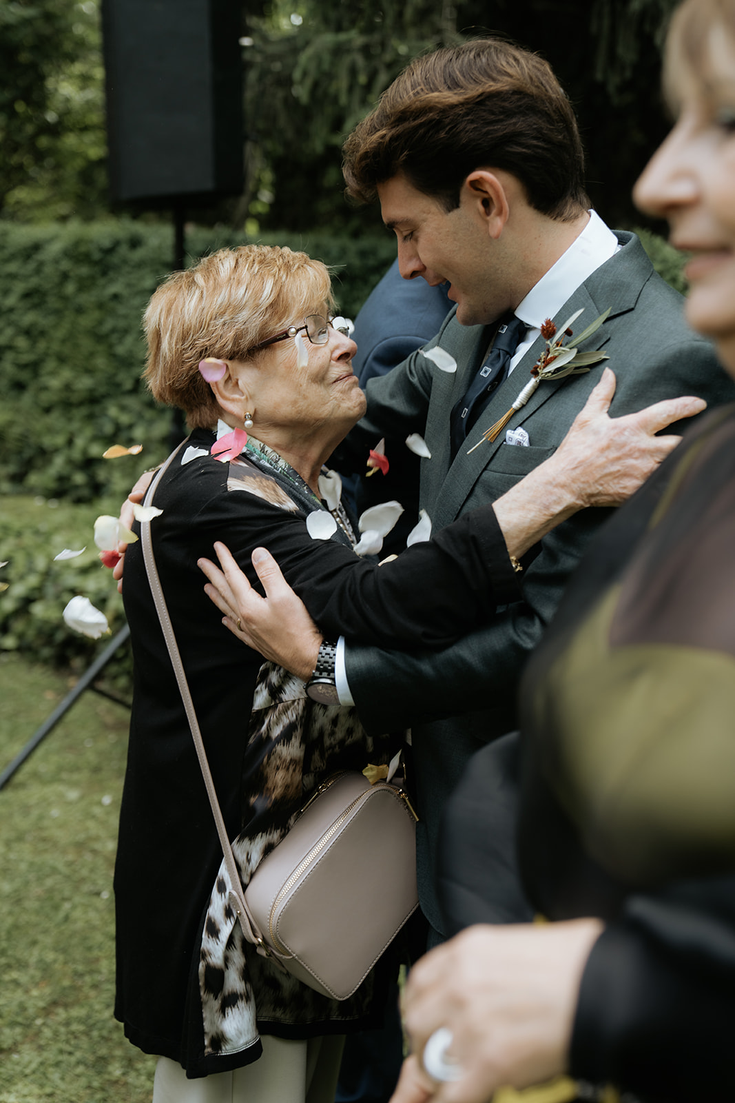 Bride in white wedding dress holding bouquet and groom in black tuxedo lying on a patterned staircase, holding hands and looking at each other.