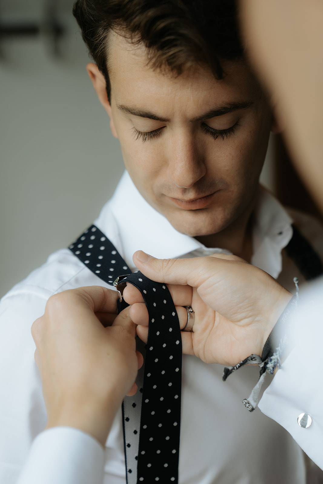 Four women in satin robes smiling and holding hands in an ornately decorated room with a wedding dress hanging in the background.