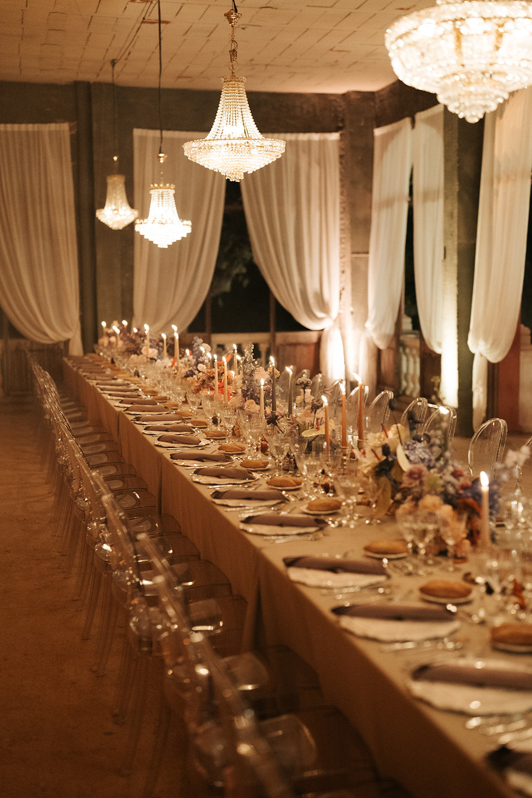 Bride in white wedding dress holding bouquet and groom in black tuxedo lying on a patterned staircase, holding hands and looking at each other.