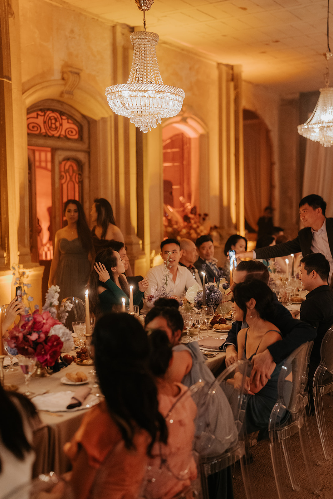 Elegant outdoor wedding setup with round tables, gold chairs, white floral arrangements, and hanging crystal chandeliers.