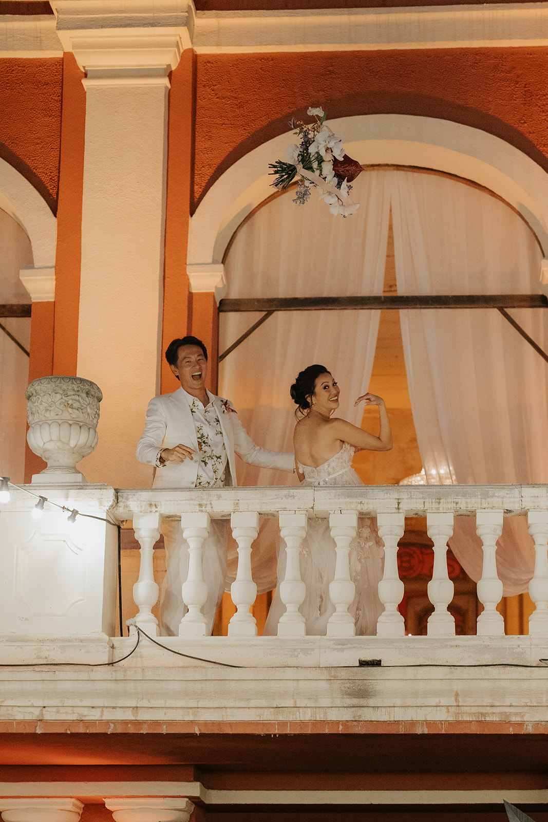 Black and white photo of a wedding party with bride and groom in the center, surrounded by bridesmaids and groomsmen on stone steps in front of an arched doorway.