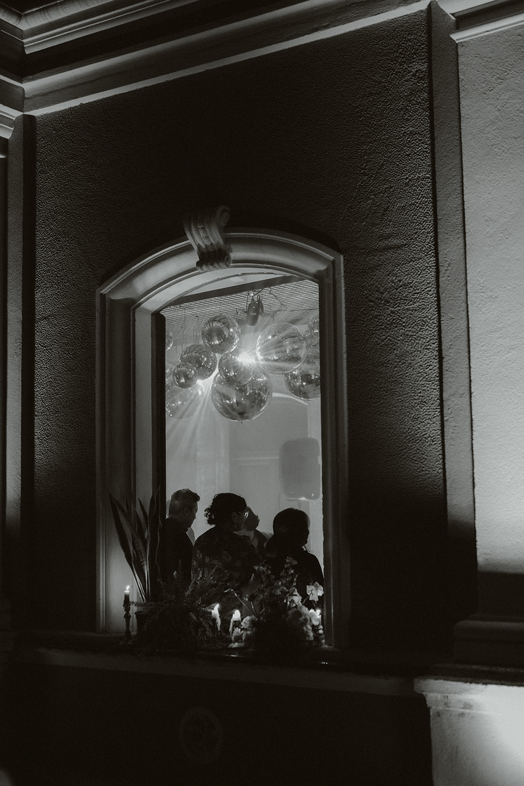 Bride and groom standing under spotlight in a grand hall surrounded by guests taking photos.