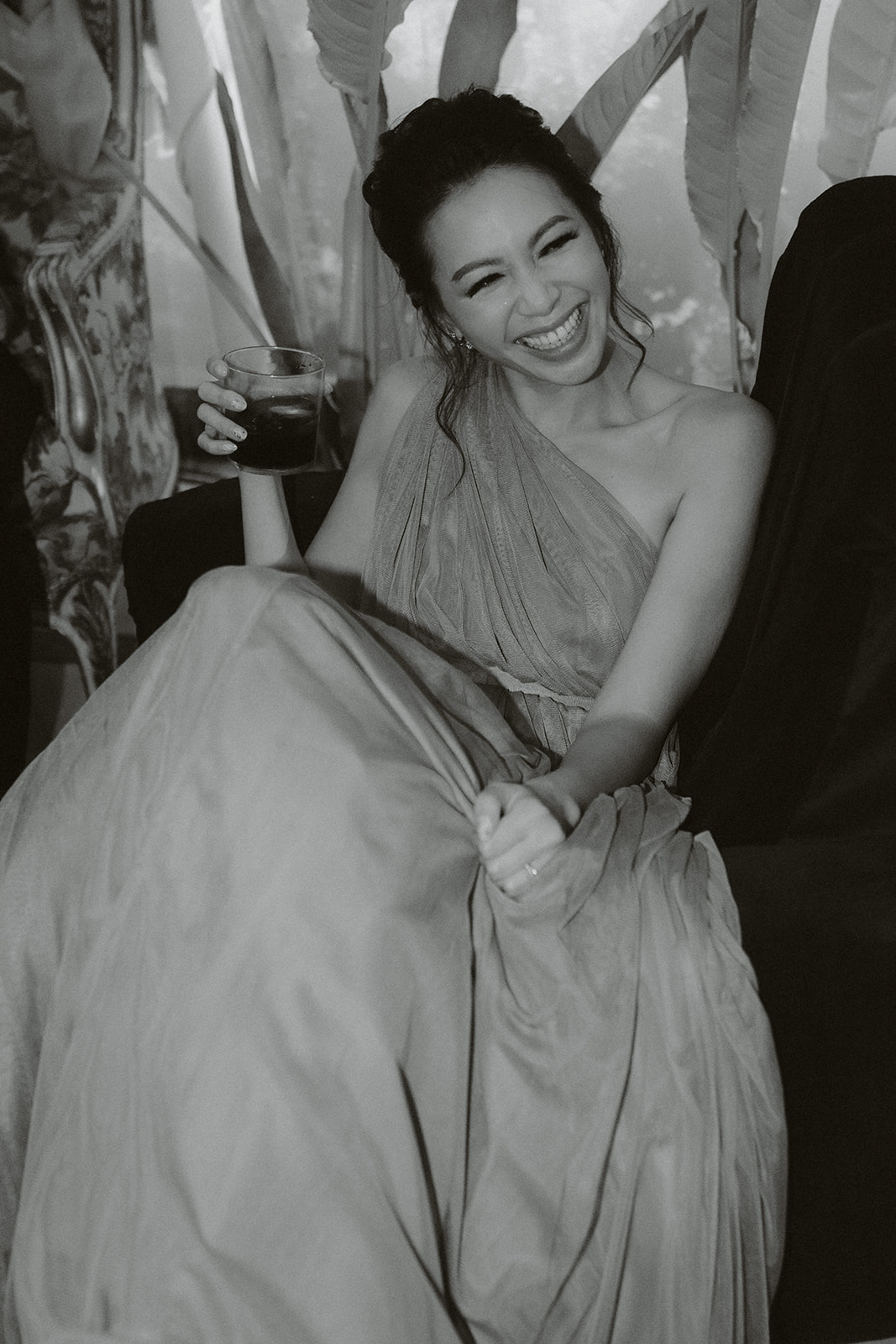 Three women in elegant dresses inside a decorated room with a chandelier, viewed through partially open doors.