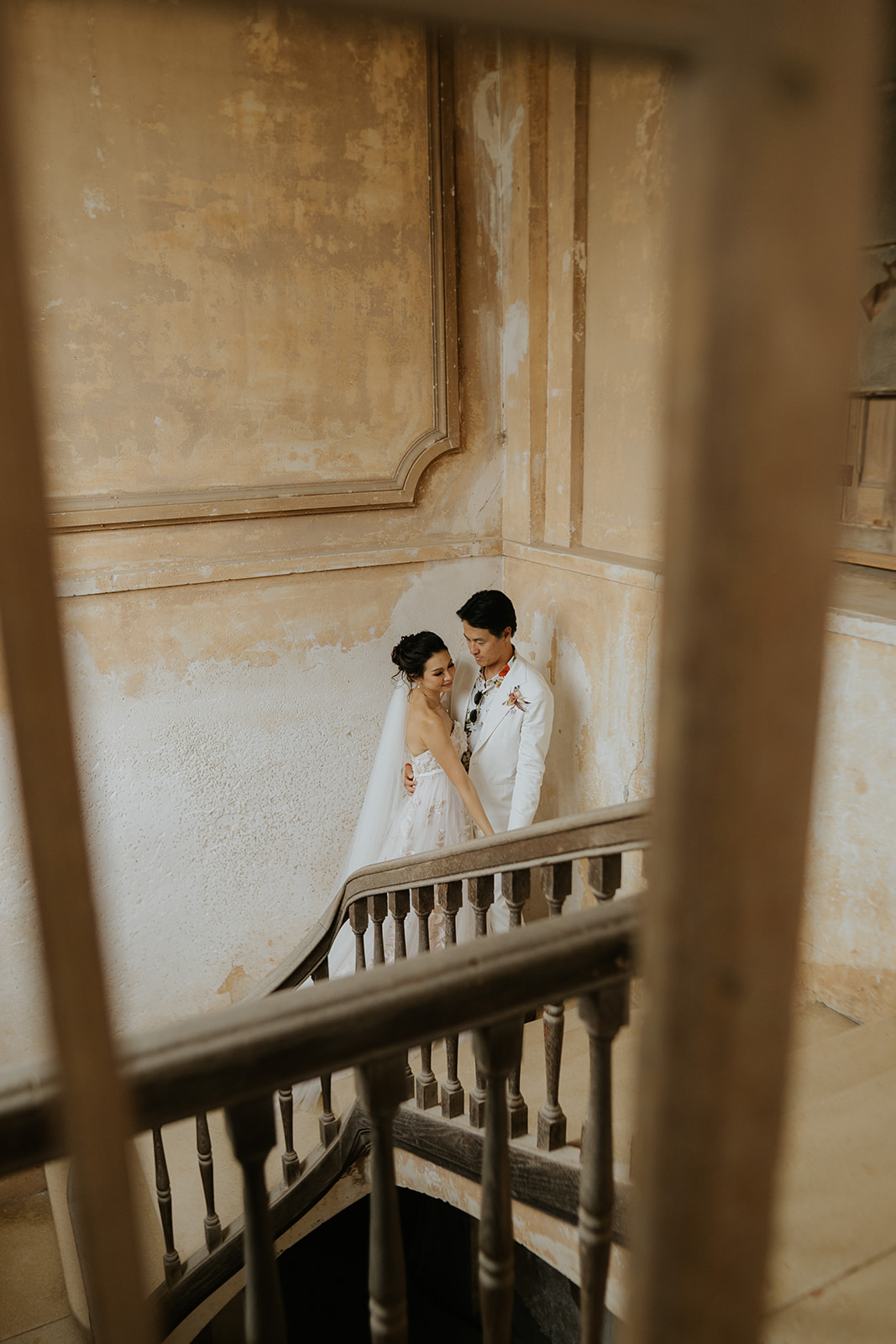 Person with manicured nails wearing gold rings resting hands on a white marble table, dressed in a white buttoned shirt.
