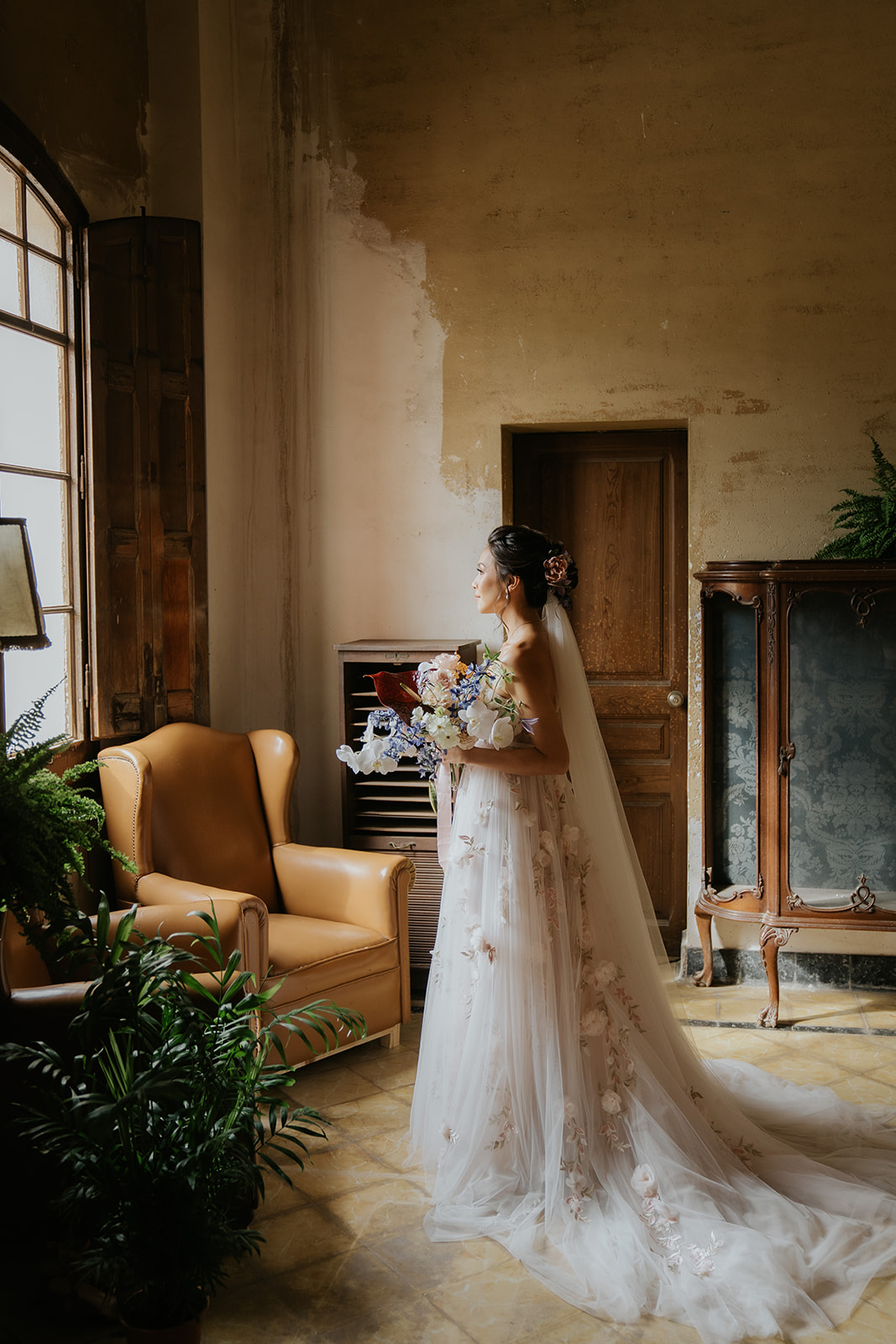 Bride and groom holding hands and smiling while walking down ornate staircase with stained glass windows and statue in the background.