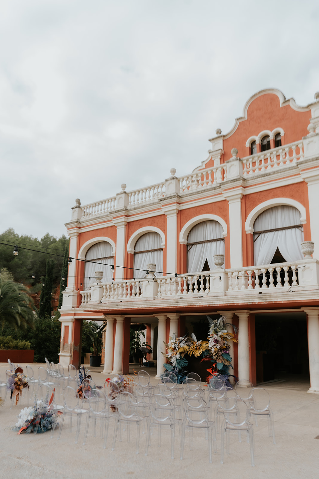 Bride and groom smiling while holding a dog dressed in a blue outfit with a smiley face collar at an indoor wedding venue.