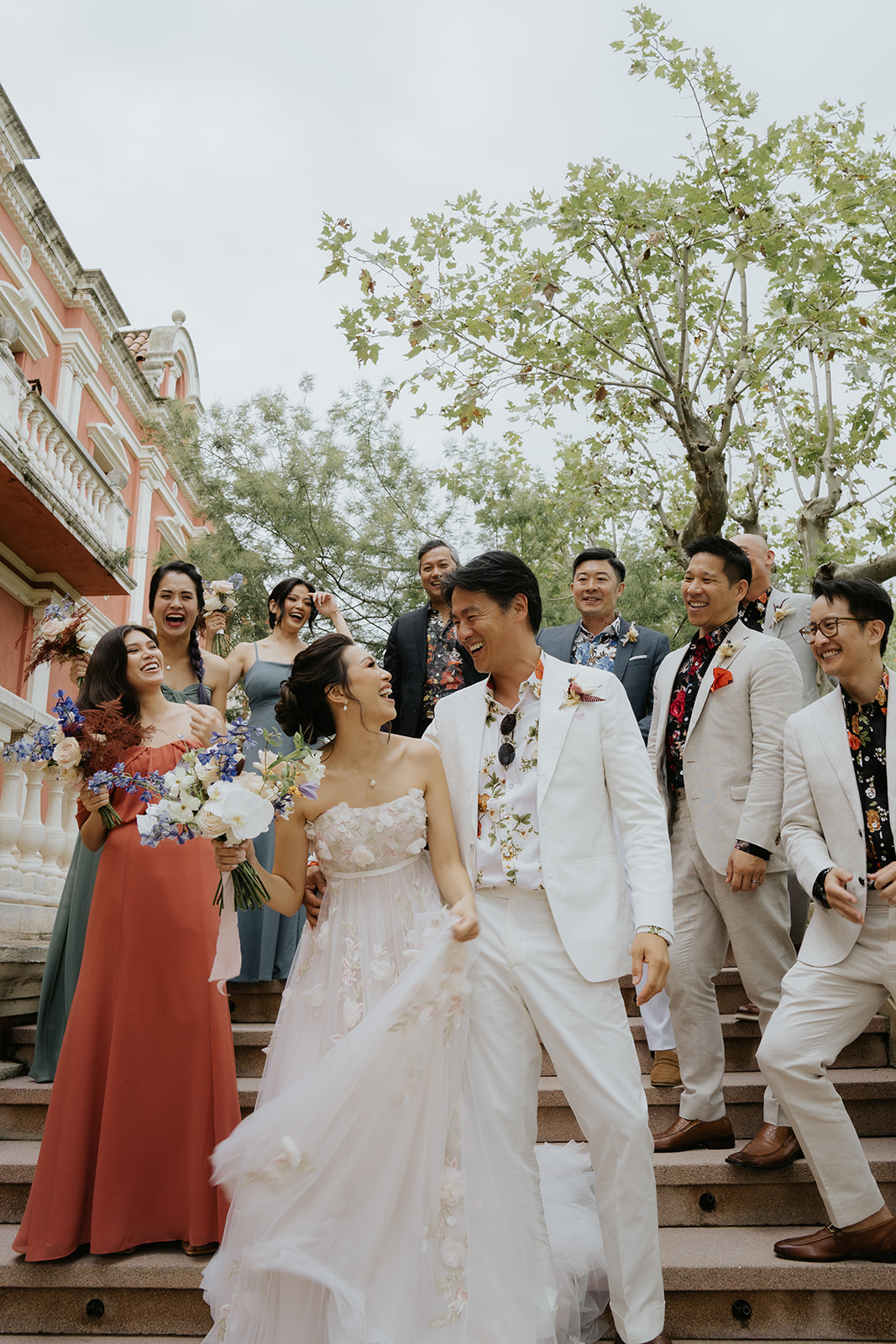 Bride and groom kissing on steps with bride holding bouquet as guests throw confetti and take photos.