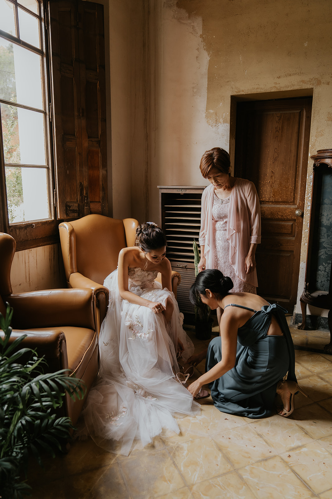Woman in silky white robe sitting on a brown couch holding a bouquet of white roses.