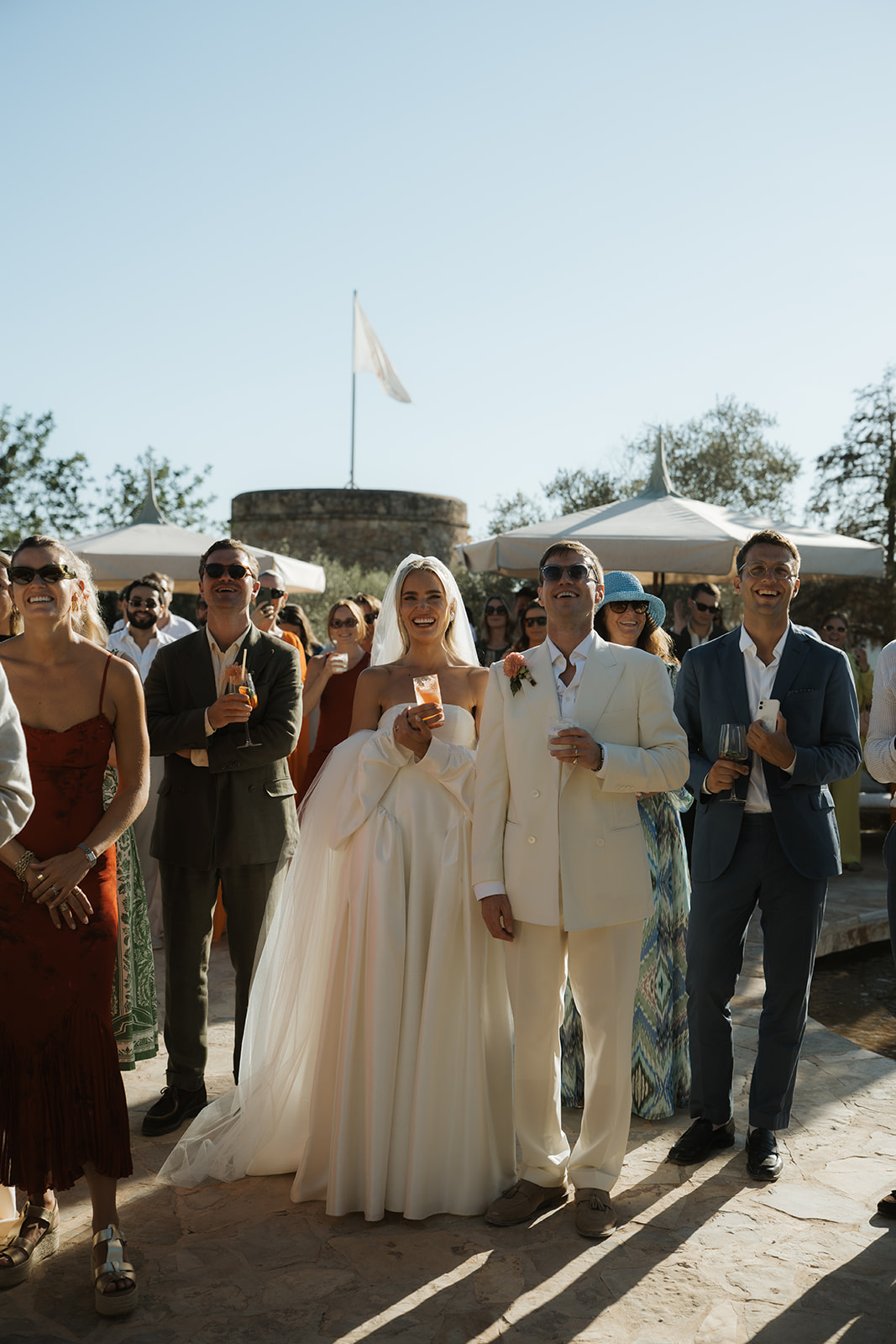 Person with manicured nails wearing gold rings resting hands on a white marble table, dressed in a white buttoned shirt.