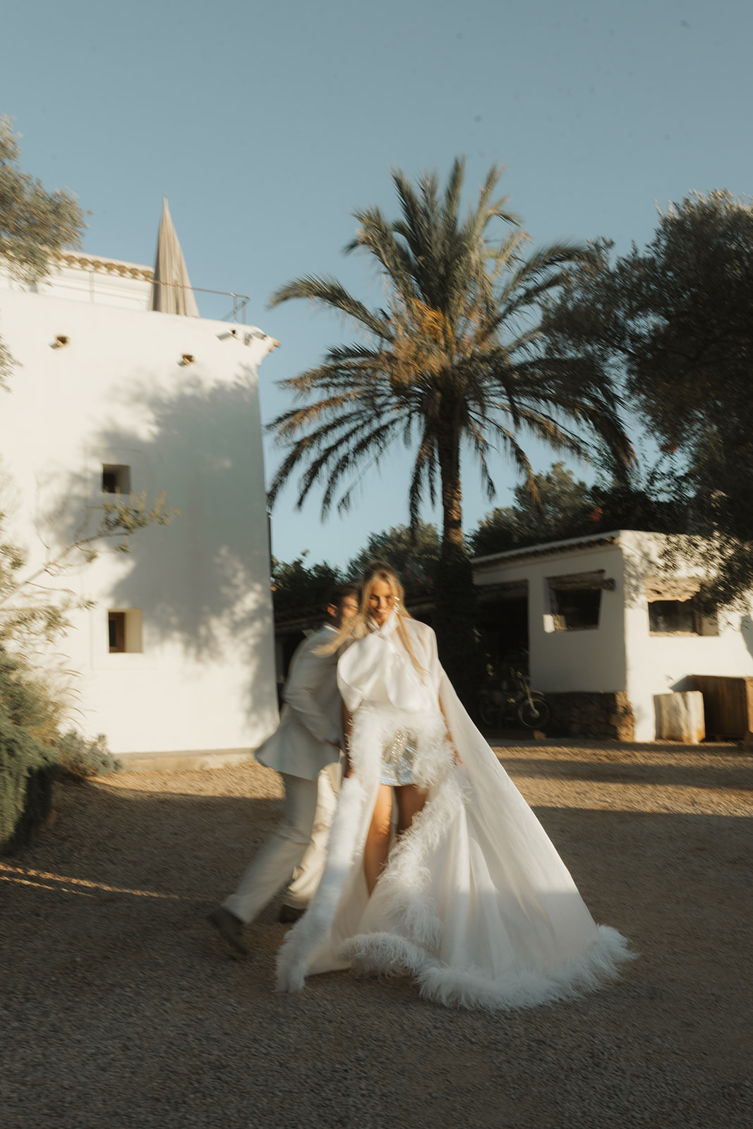 Bride and groom standing under spotlight in a grand hall surrounded by guests taking photos.