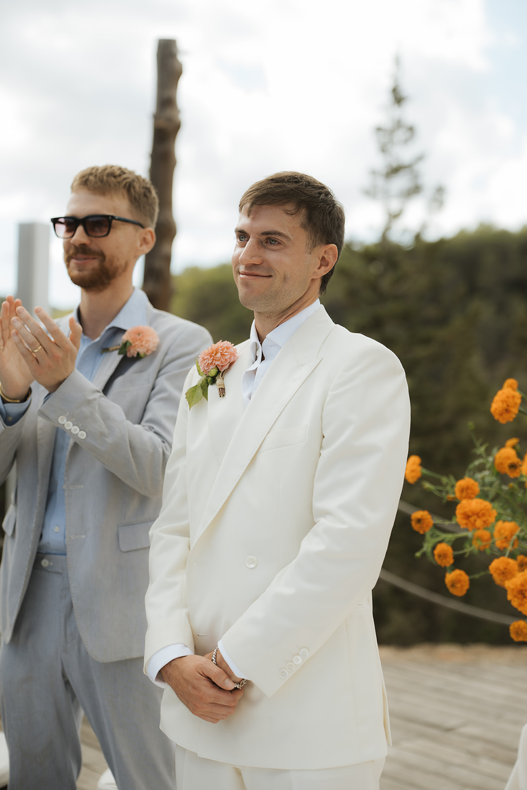 Bride and groom smiling while holding a dog dressed in a blue outfit with a smiley face collar at an indoor wedding venue.