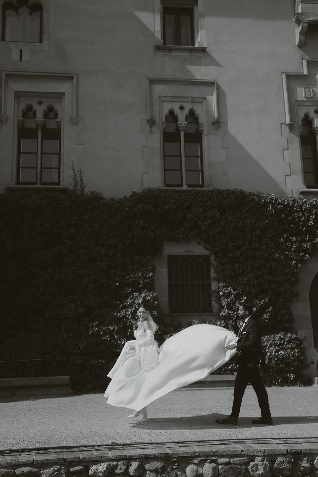 Bride and groom holding hands and smiling while walking down ornate staircase with stained glass windows and statue in the background.