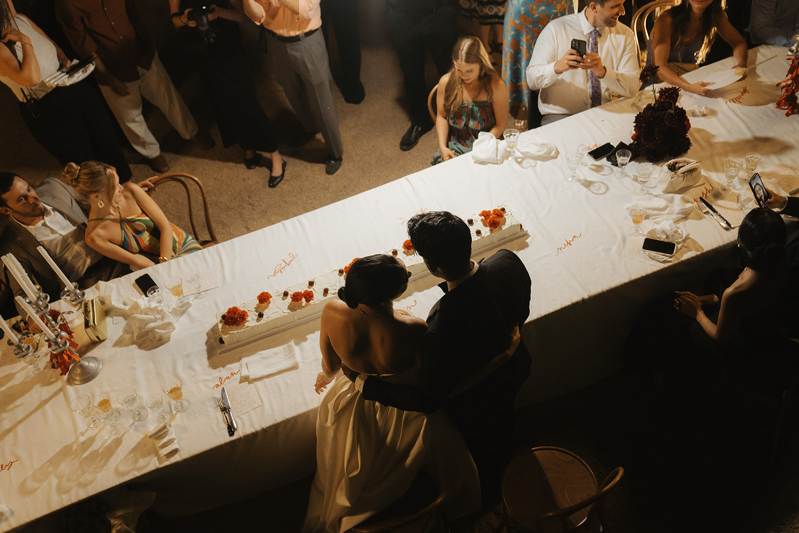 Black and white photo of a man adjusting his formal shirt and bow tie while looking at his reflection in an oval mirror.