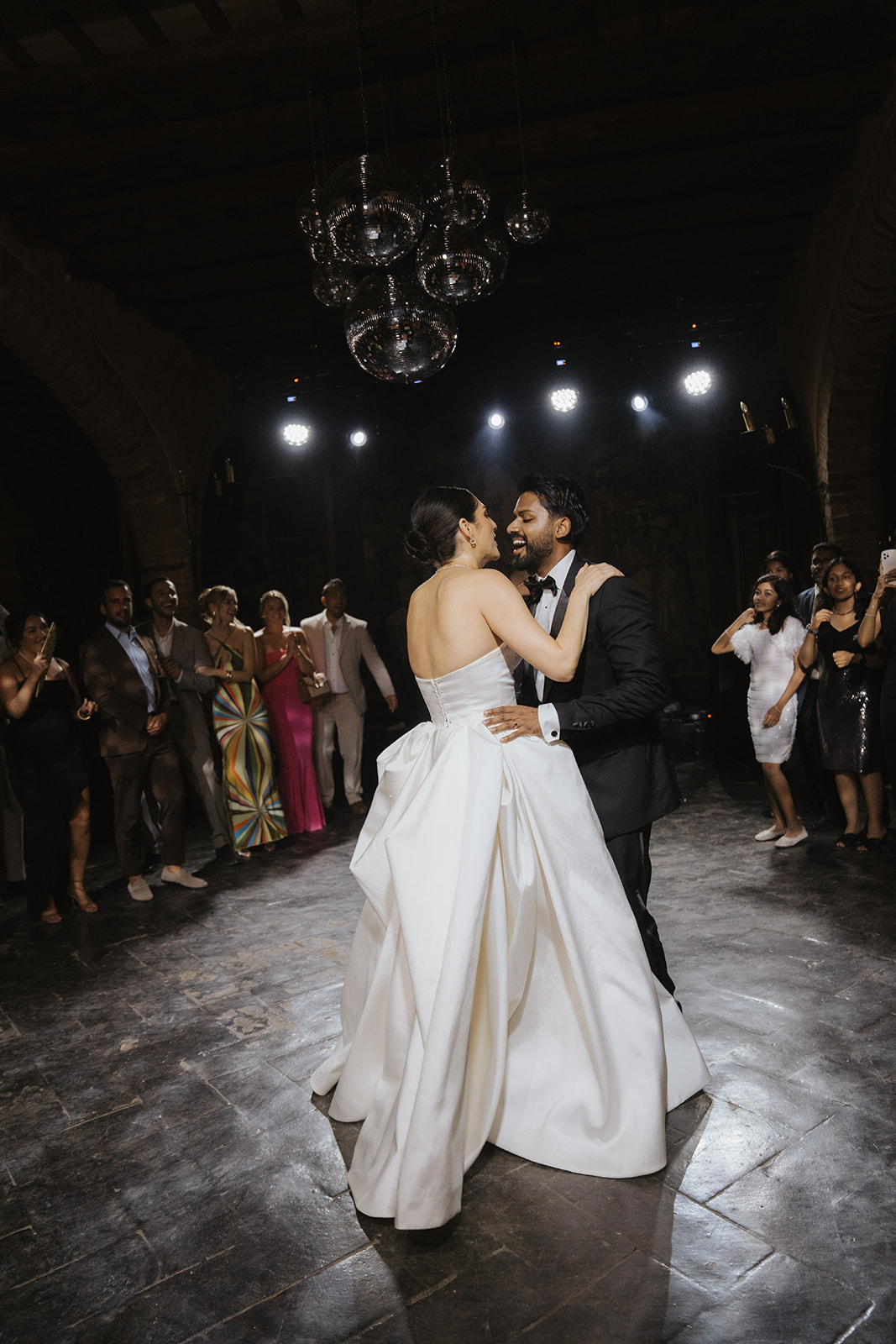 Black and white photo of a wedding party with bride and groom in the center, surrounded by bridesmaids and groomsmen on stone steps in front of an arched doorway.