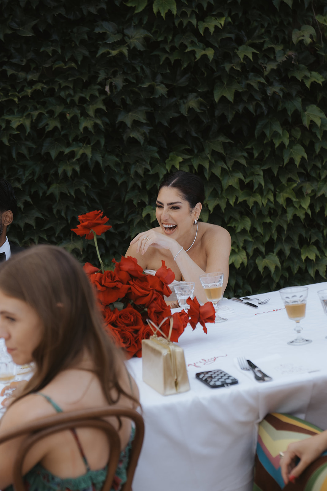Four women in satin robes smiling and holding hands in an ornately decorated room with a wedding dress hanging in the background.
