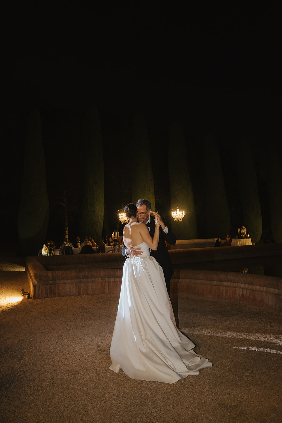 Black and white photo of a couple embracing during a dance in a dimly lit venue with a bright light above.