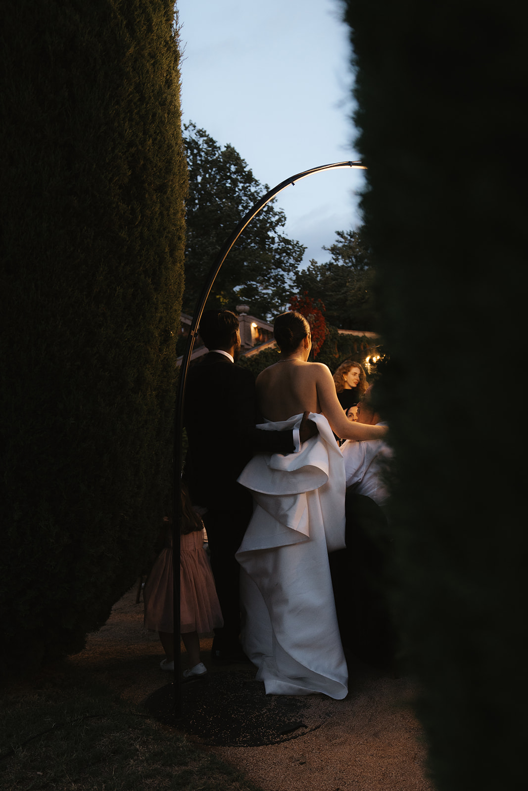Bride in white wedding dress holding bouquet and groom in black tuxedo lying on a patterned staircase, holding hands and looking at each other.