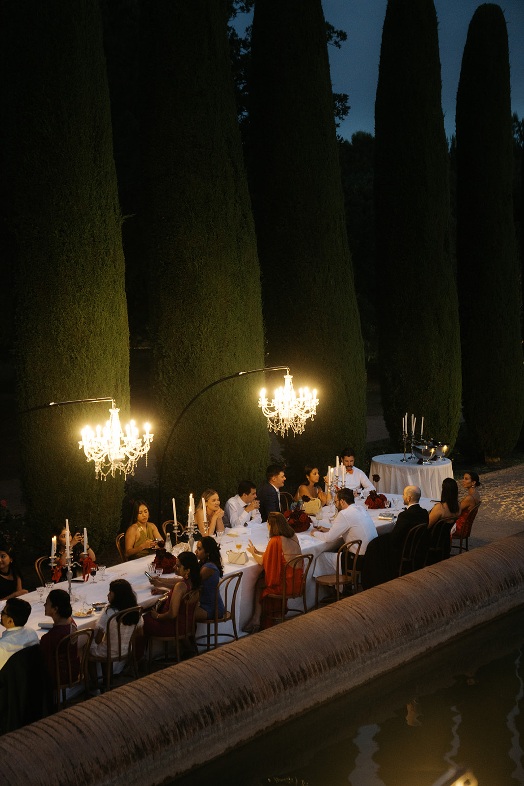 Bride and groom standing under spotlight in a grand hall surrounded by guests taking photos.