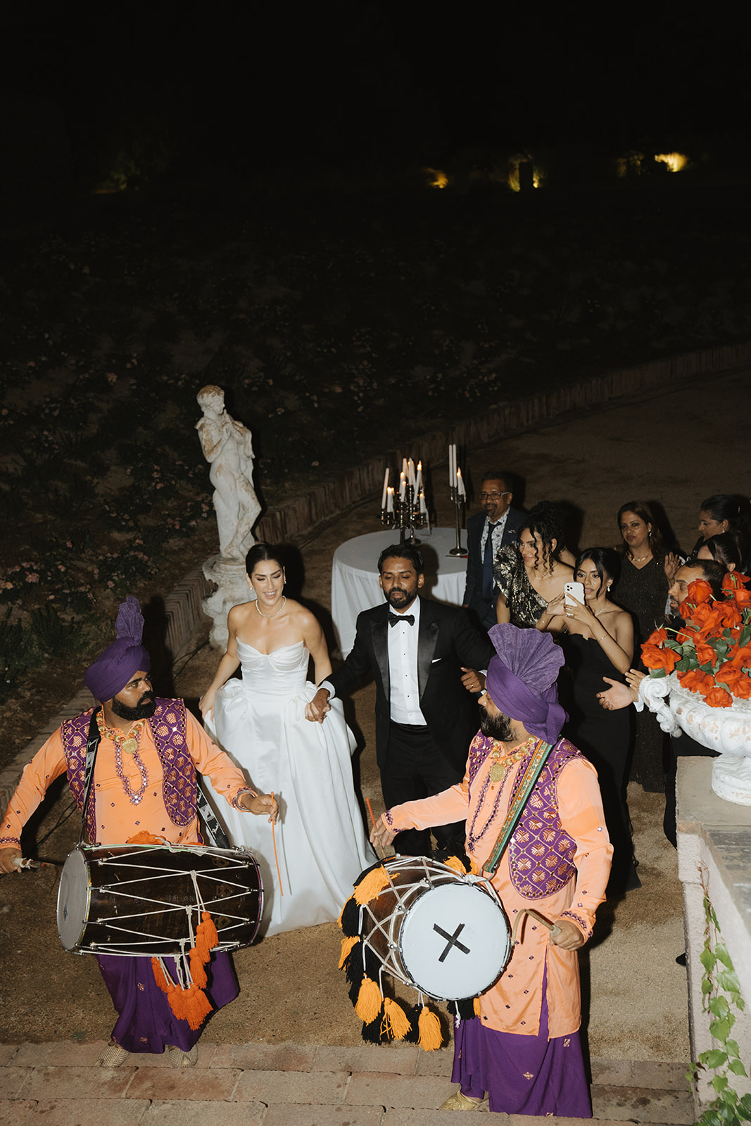 Person with manicured nails wearing gold rings resting hands on a white marble table, dressed in a white buttoned shirt.