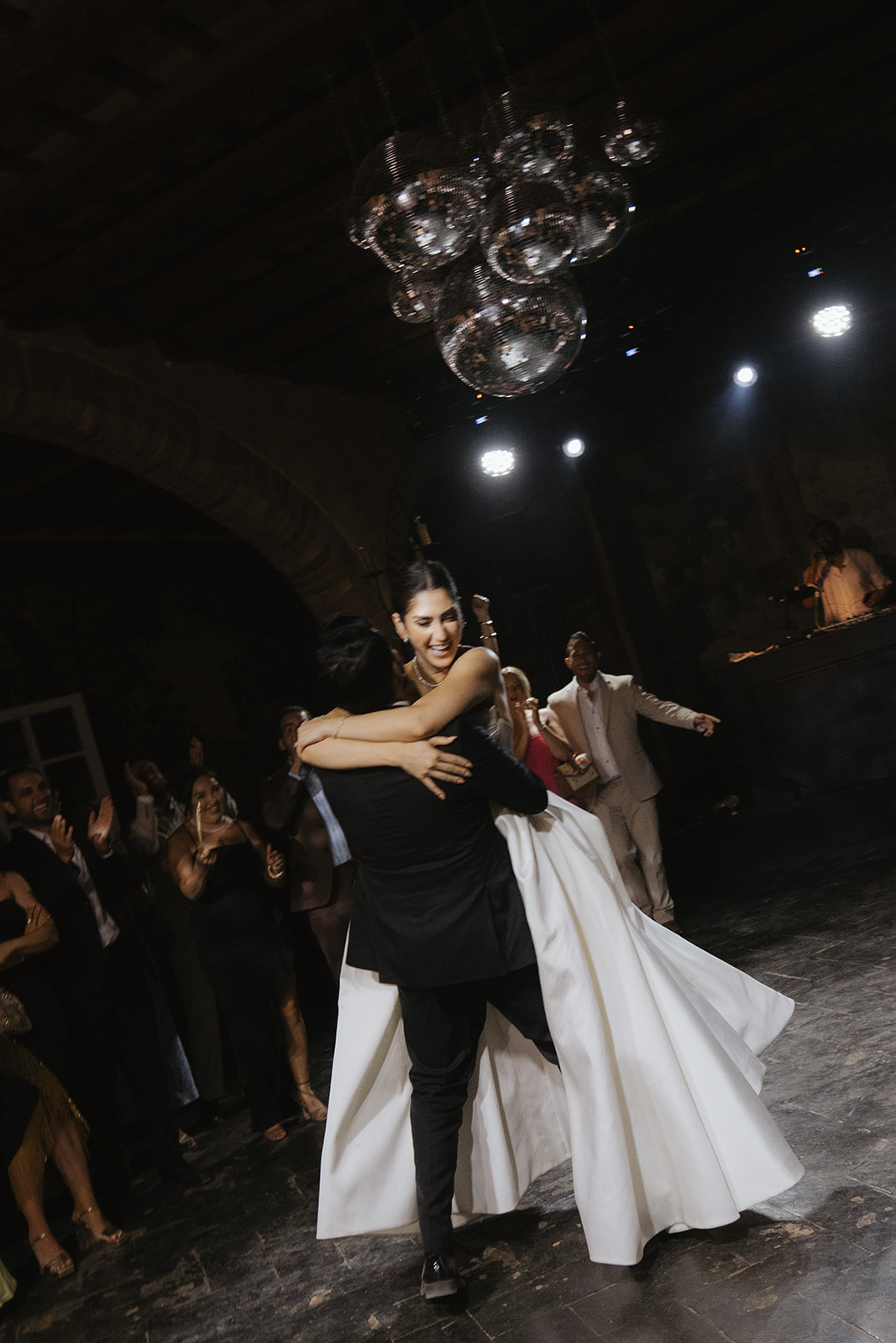Three women in elegant dresses inside a decorated room with a chandelier, viewed through partially open doors.