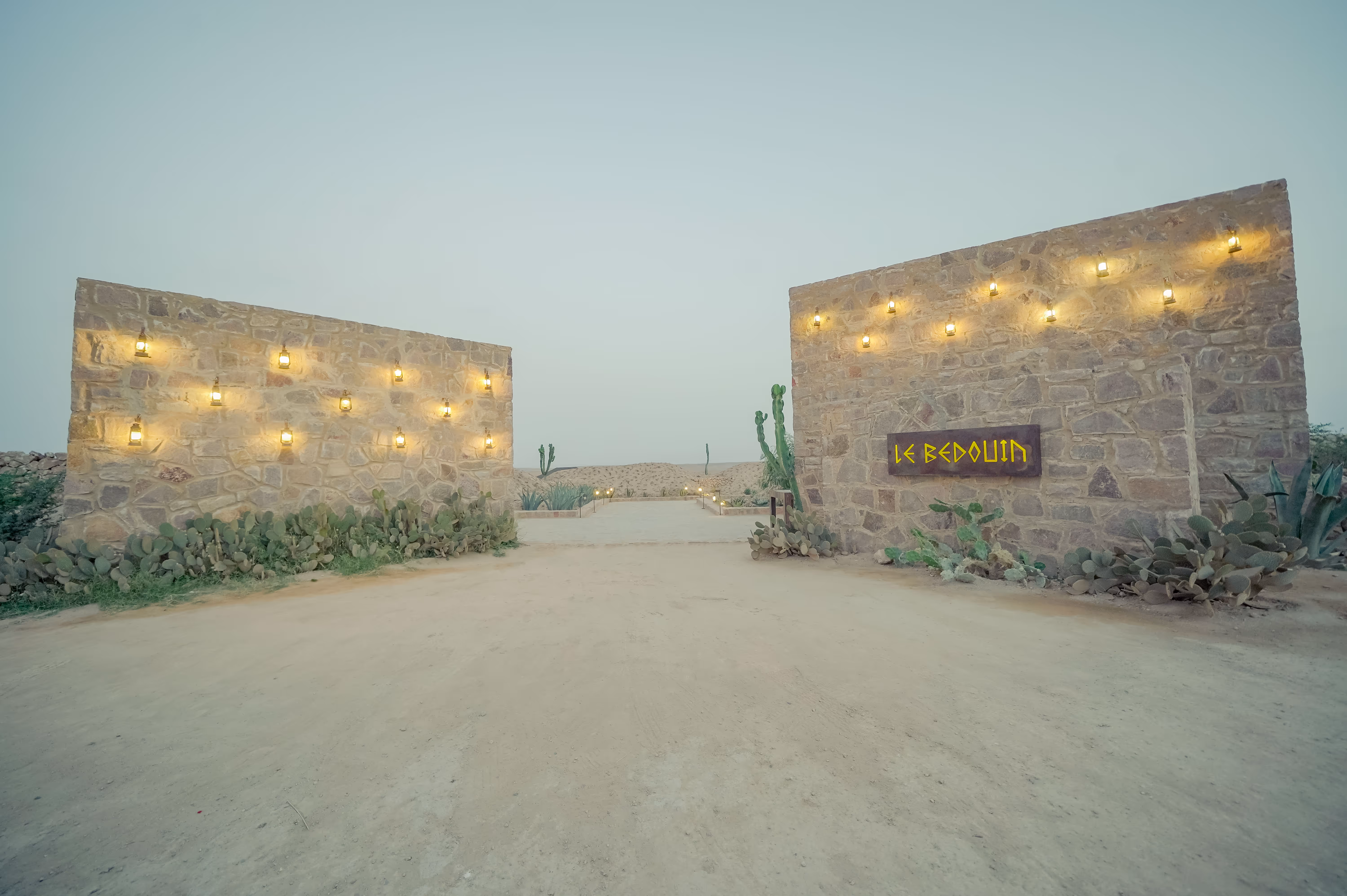 Person dressed in white walking barefoot between intricately tiled columns reflected in a calm pool.