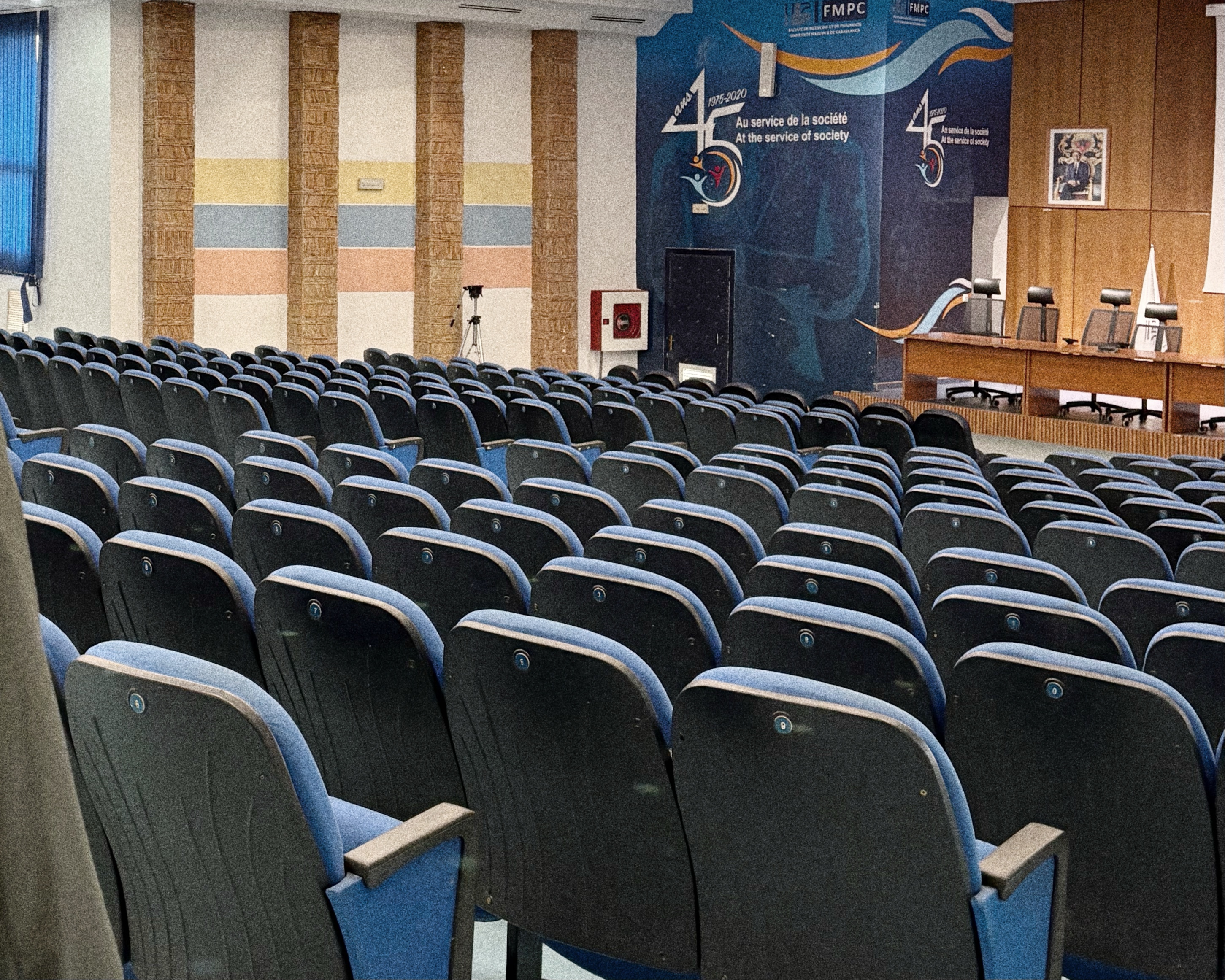 Conference room with rows of patterned chairs, red carpet, chandeliers, and a presentation screen displaying Le Casablanca Hotel logo.