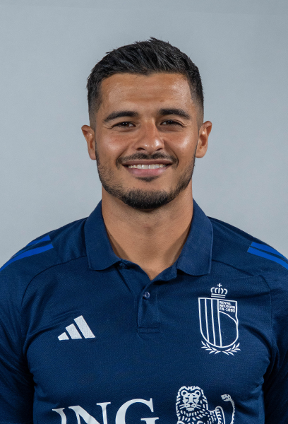 Smiling female doctor wearing a white lab coat over navy scrubs against a gray background.