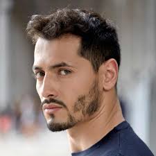 Smiling female doctor wearing a white lab coat over navy scrubs against a gray background.
