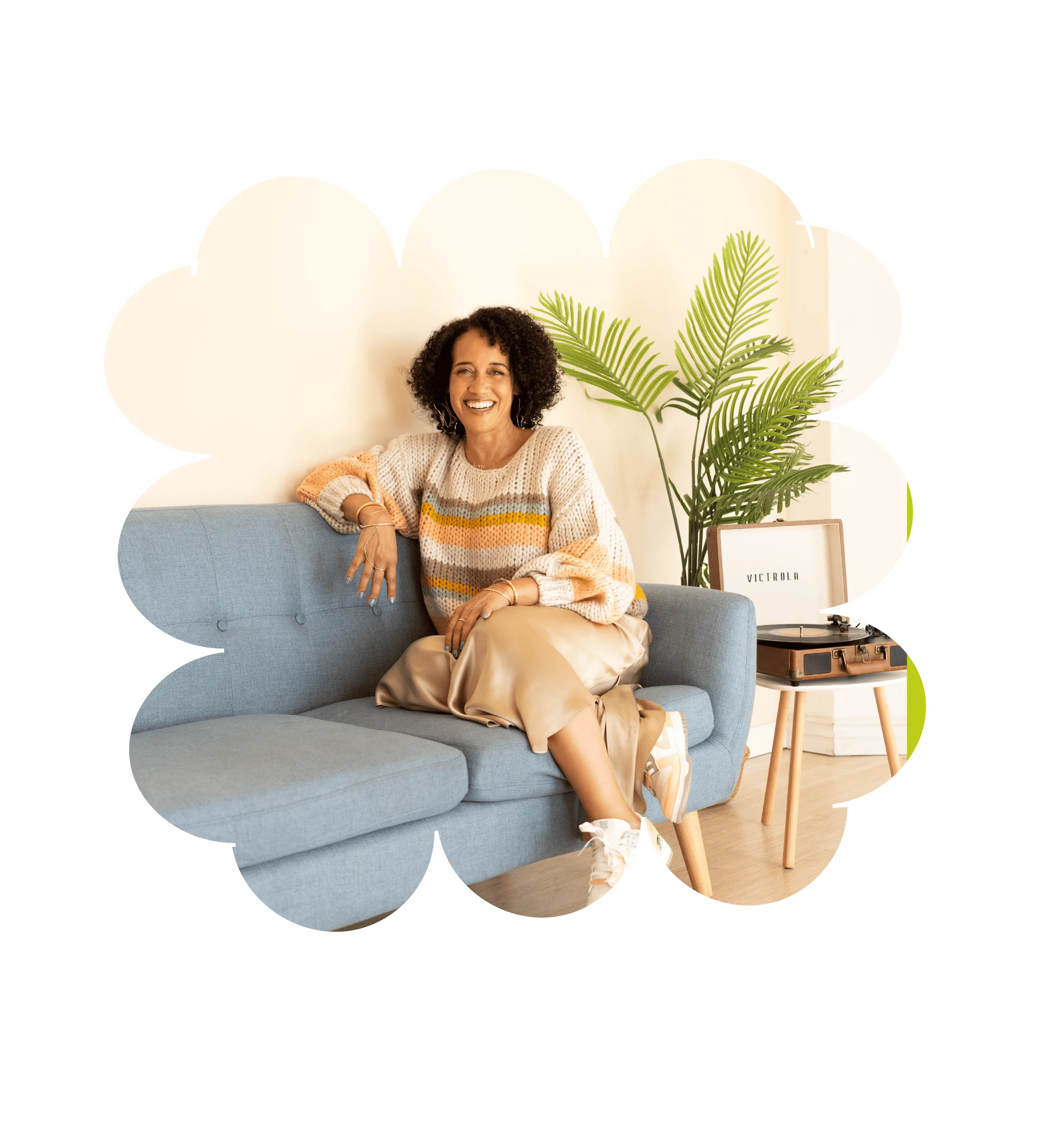 Smiling woman in a cozy sweater sitting on a blue couch with a record player and plant nearby.