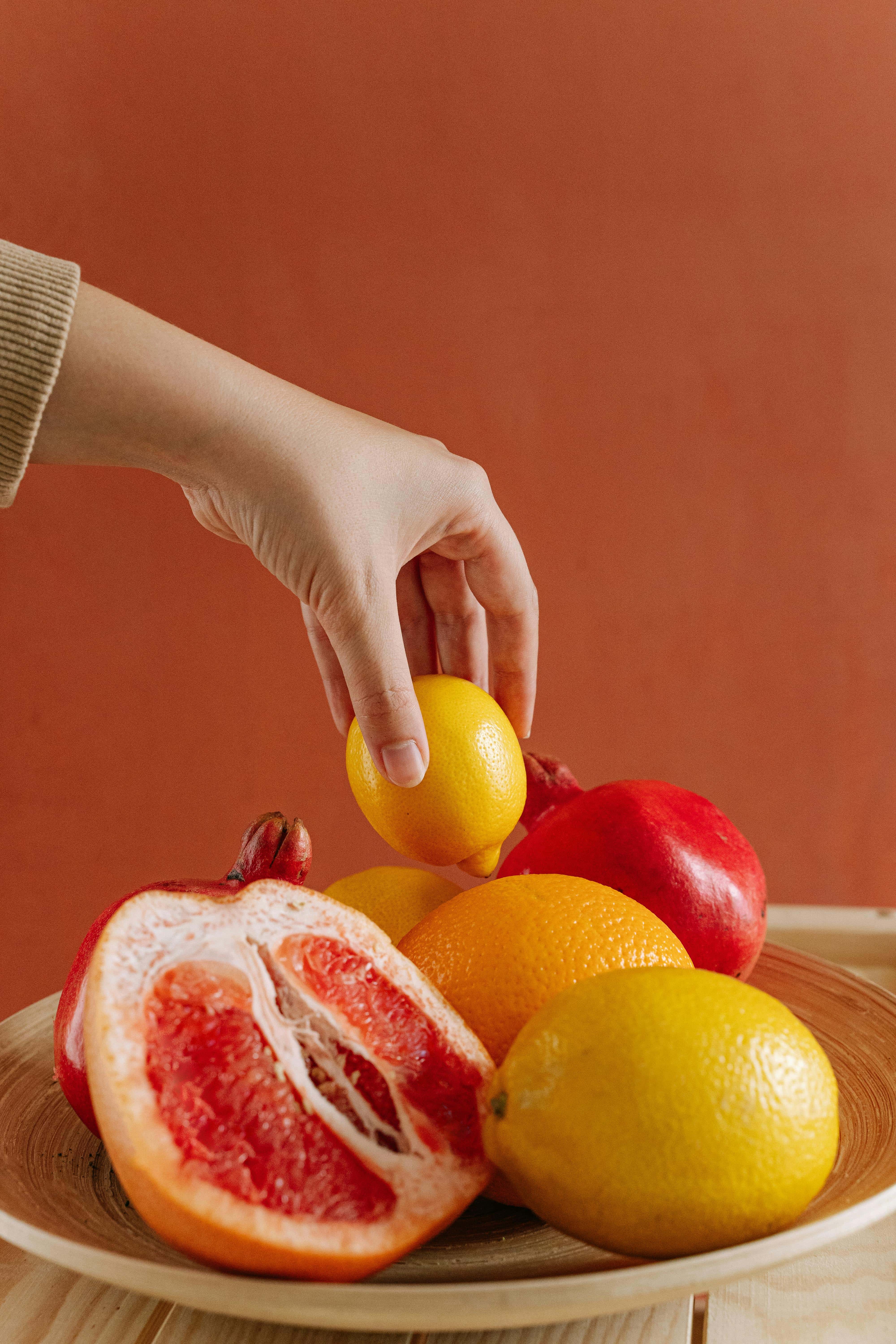 a feminine hand picking a lemon from a bowl of fruits