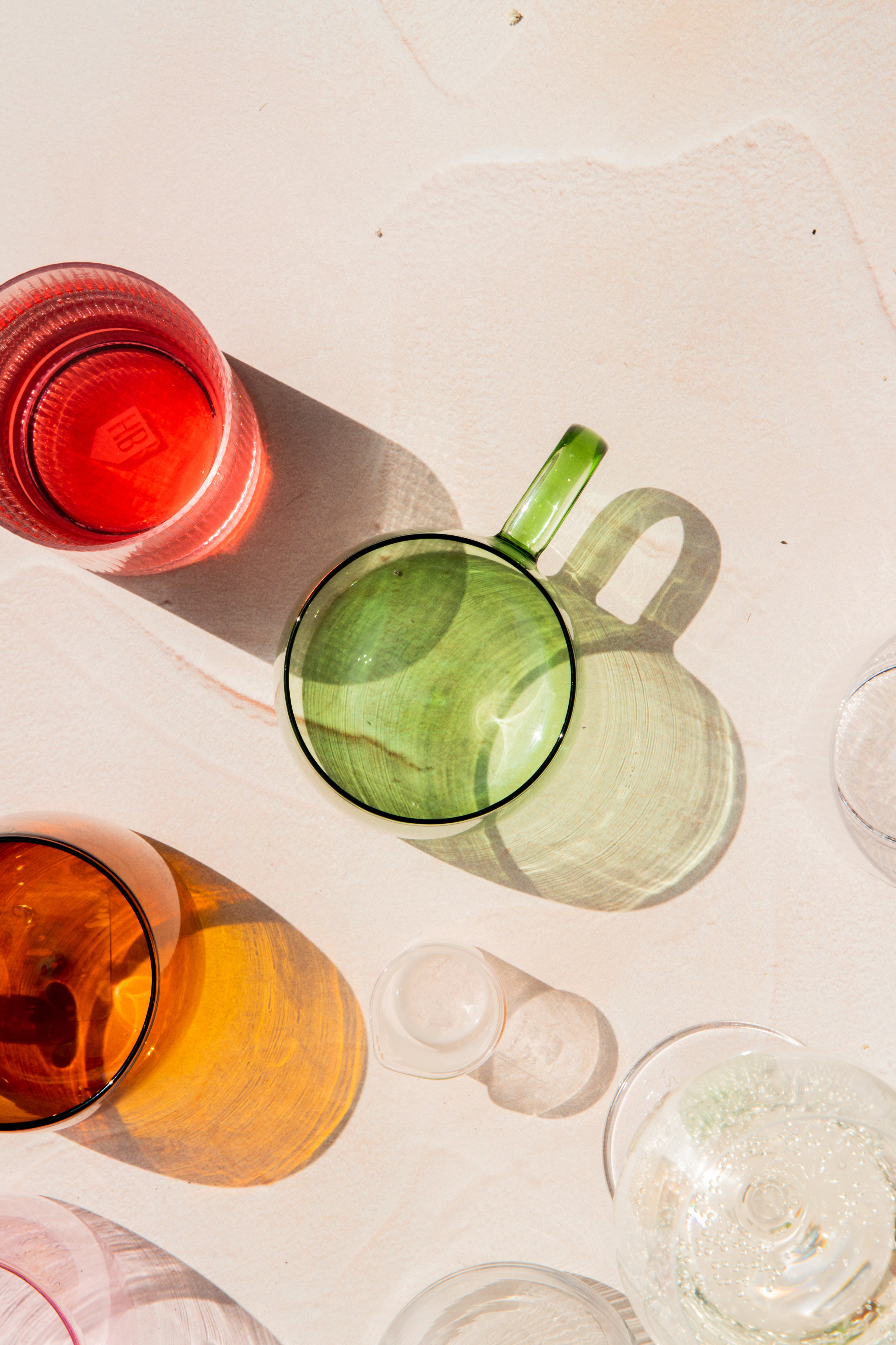 Overhead view of colorful glass cups and a green mug casting shadows on a light surface.