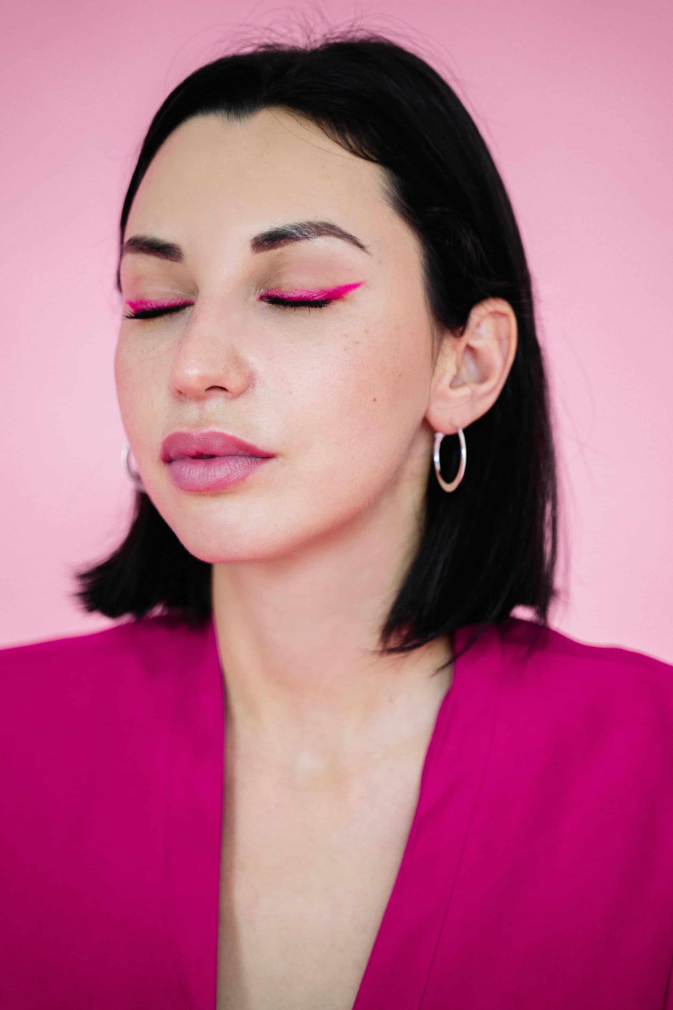 woman with bright eye makeup and hoop earrings closing her eyes