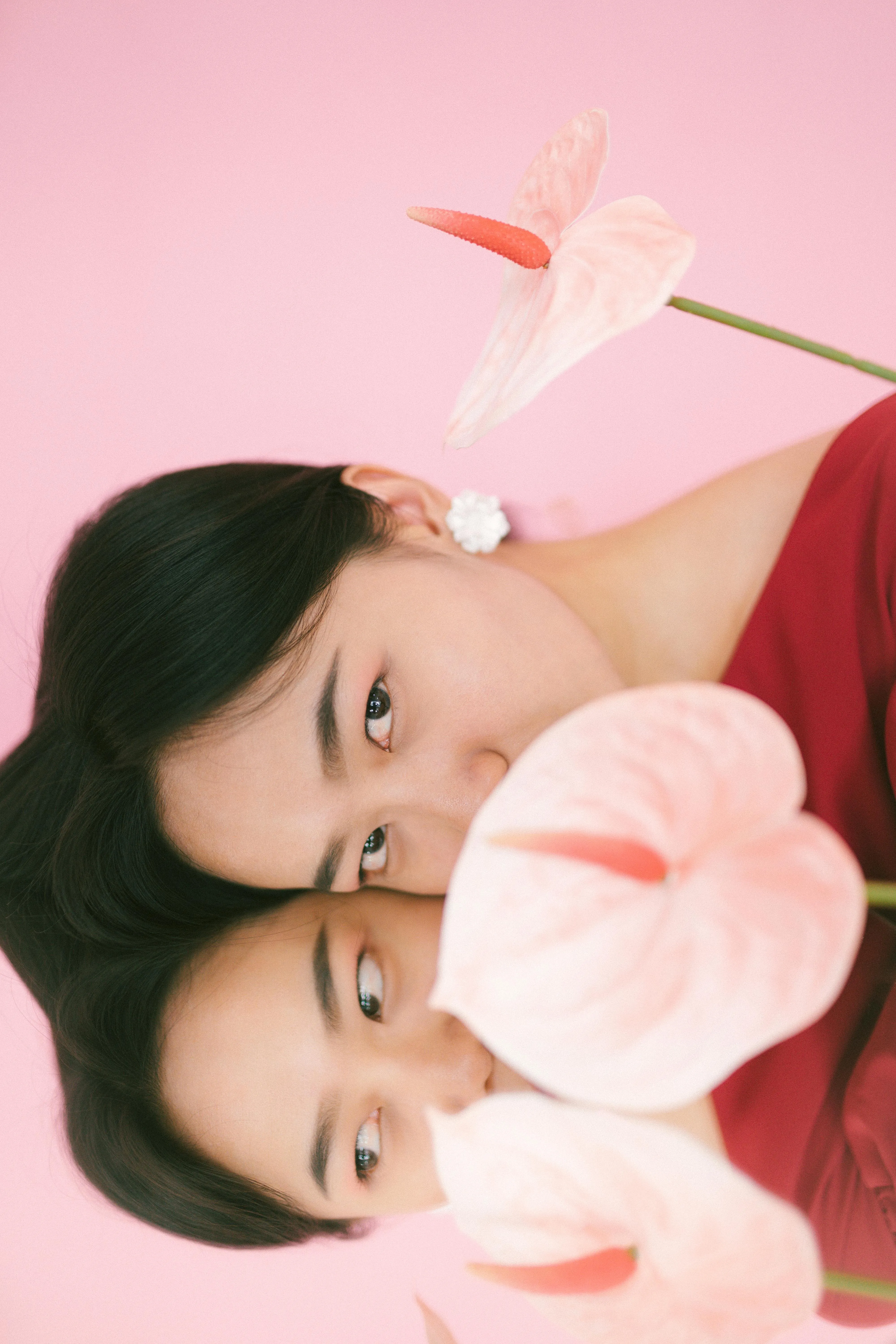 Smiling elderly woman with white hair wearing round black glasses, a pink hat, white shirt, and brown checkered dress.
