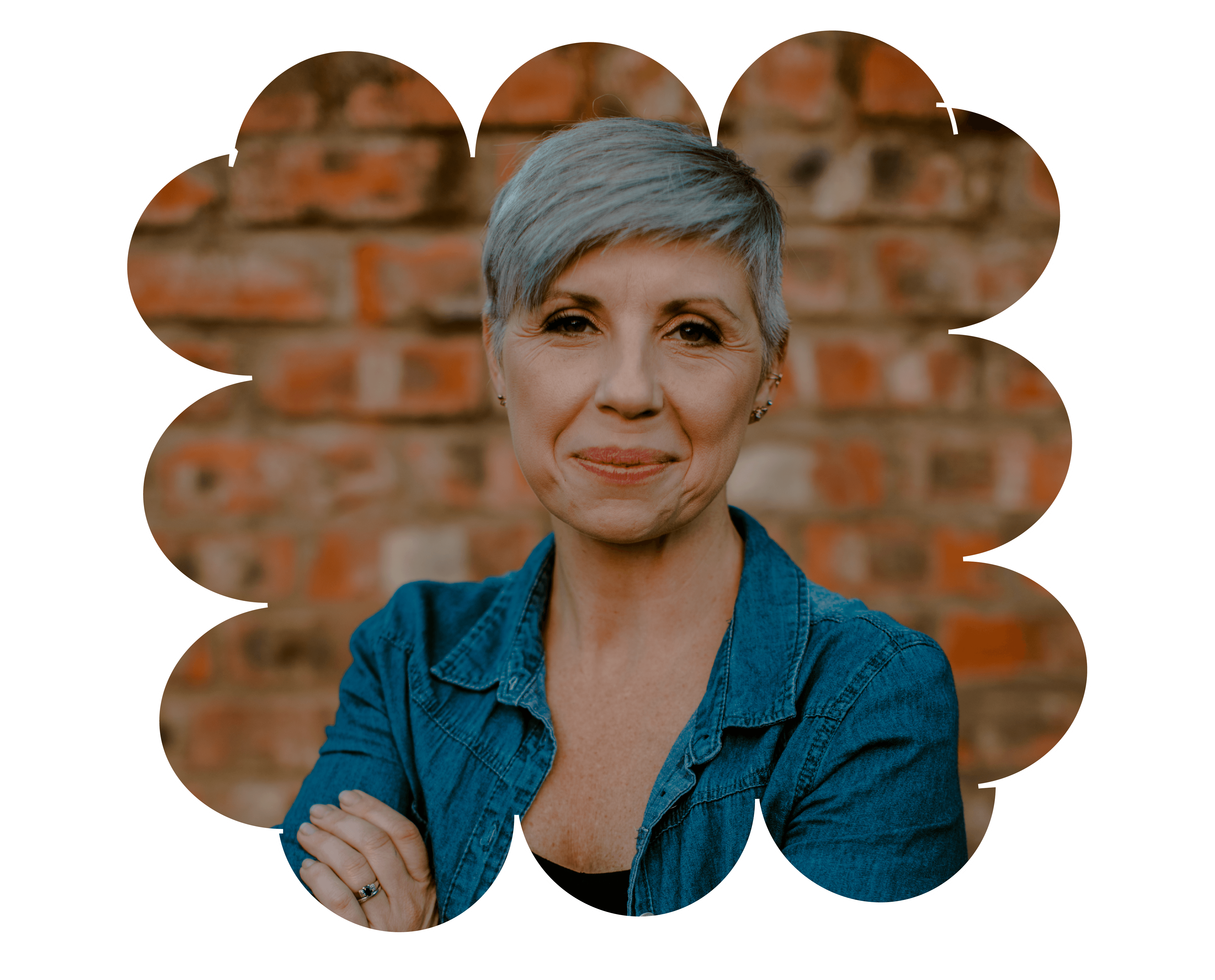 Smiling middle-aged woman with short gray hair wearing a denim jacket against a brick wall.