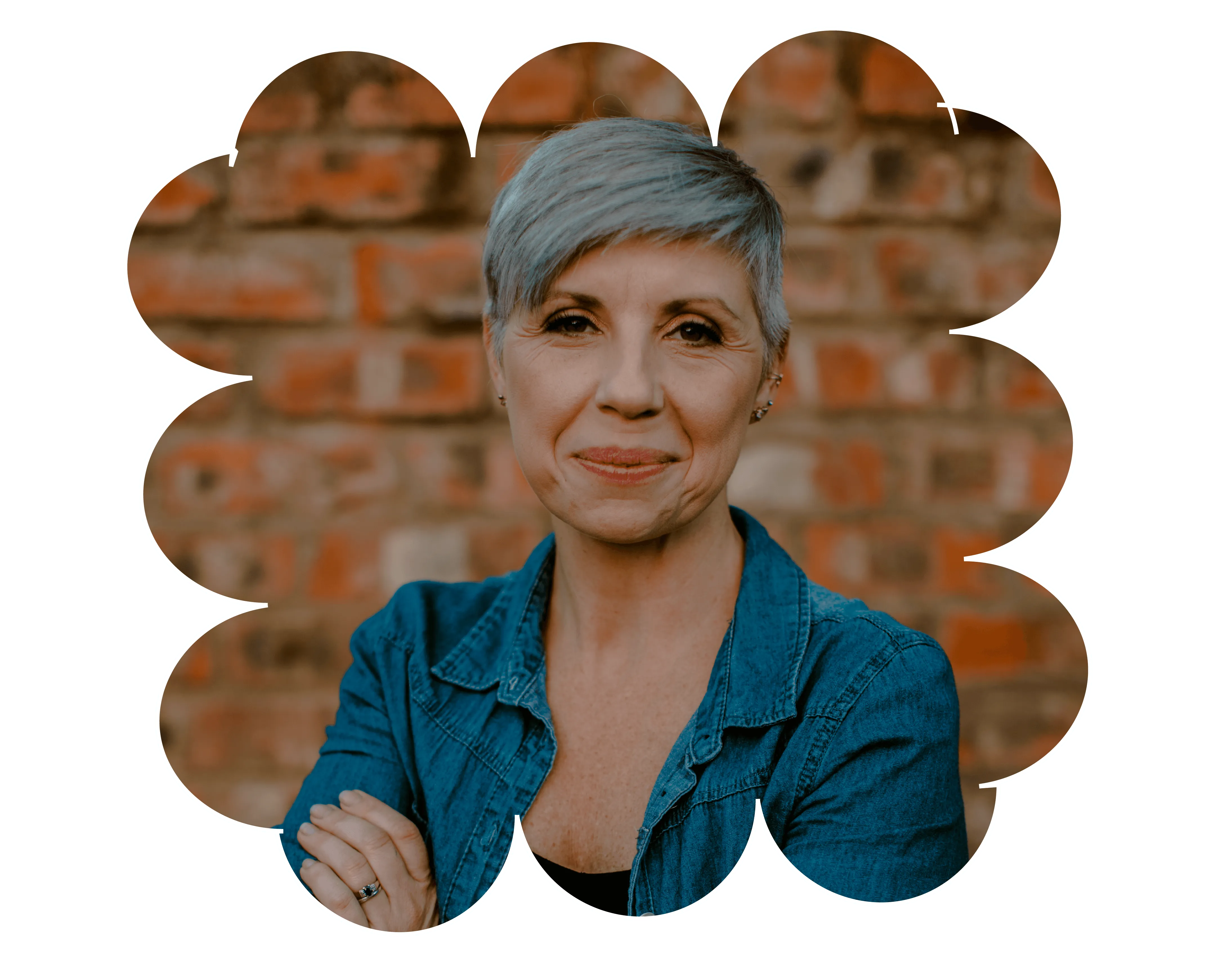 Smiling middle-aged woman with short gray hair wearing a denim jacket against a brick wall.