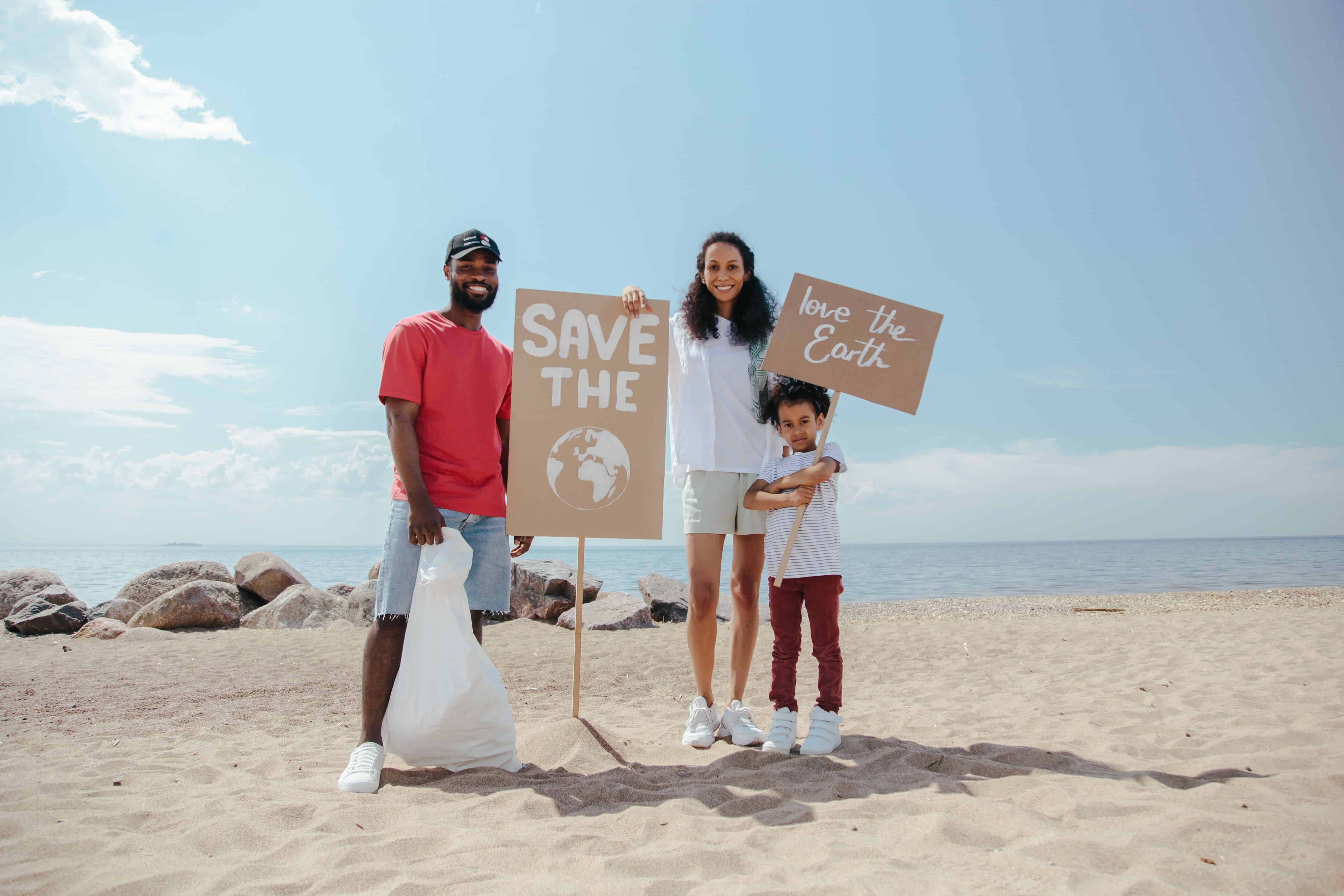 Family on beach holding signs saying 'Save the Earth' and 'Love the Earth' during cleanup.