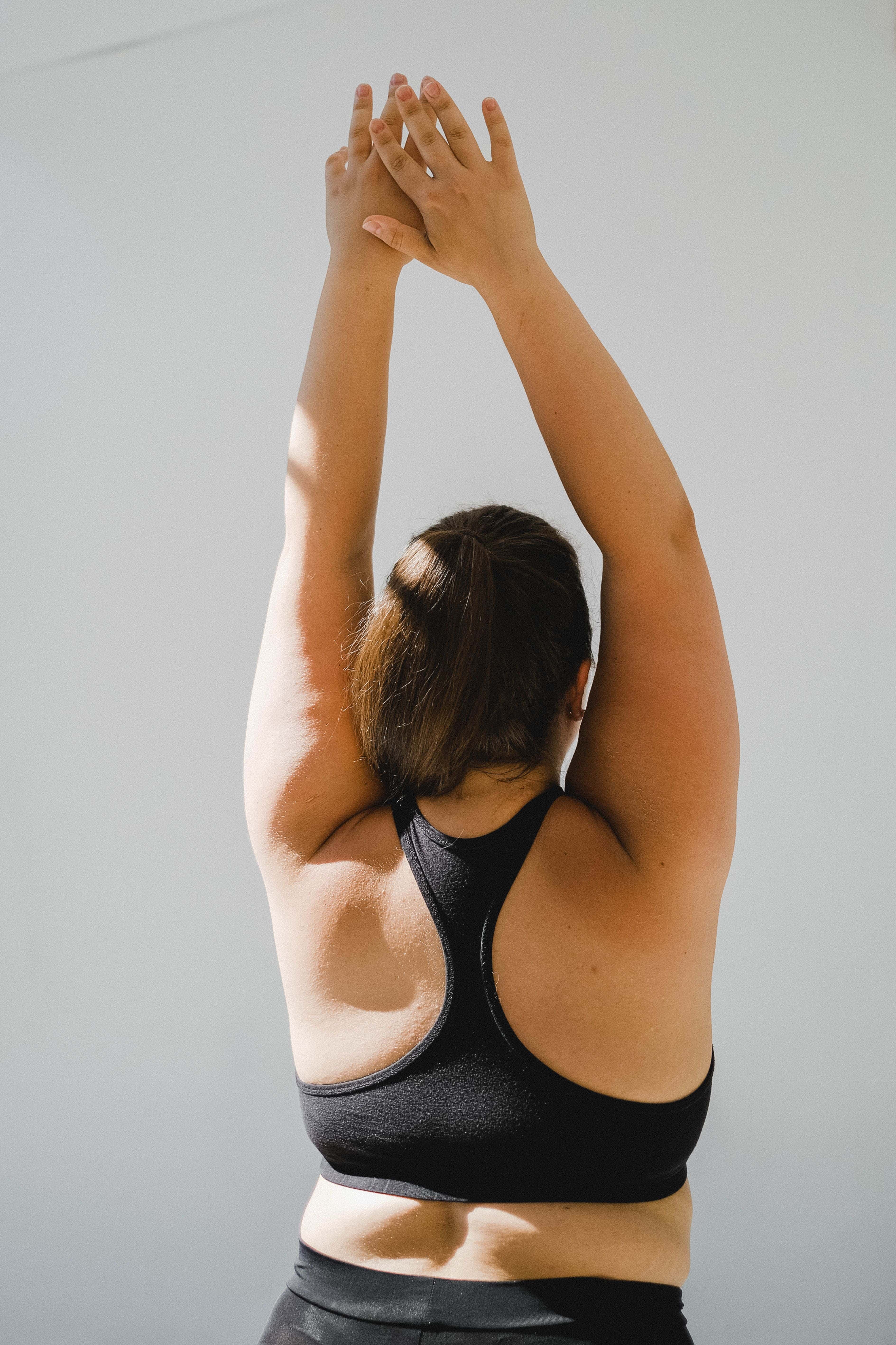 Woman in black sportswear stretching arms upward against plain light background.