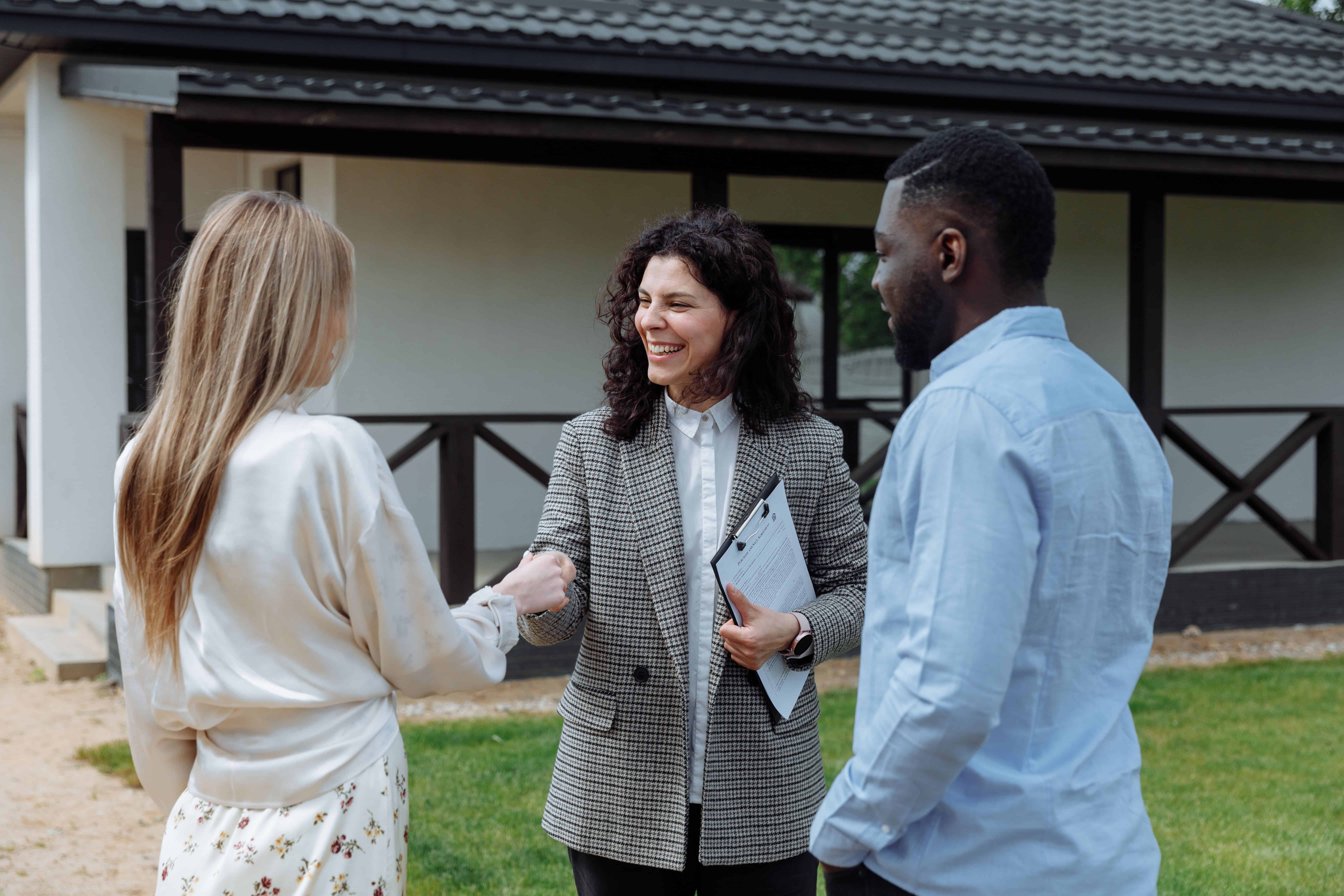 Real estate agent shaking hands with a couple in front of a house on a lawn.