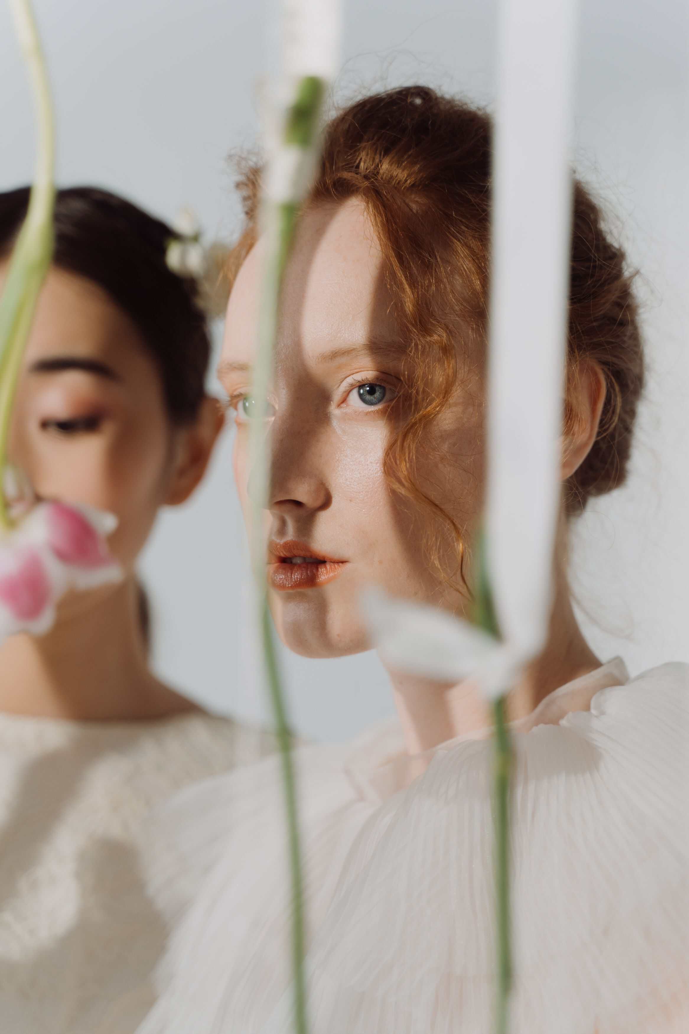 Woman with red hair wearing a sheer white blouse among hanging pink and white flowers.