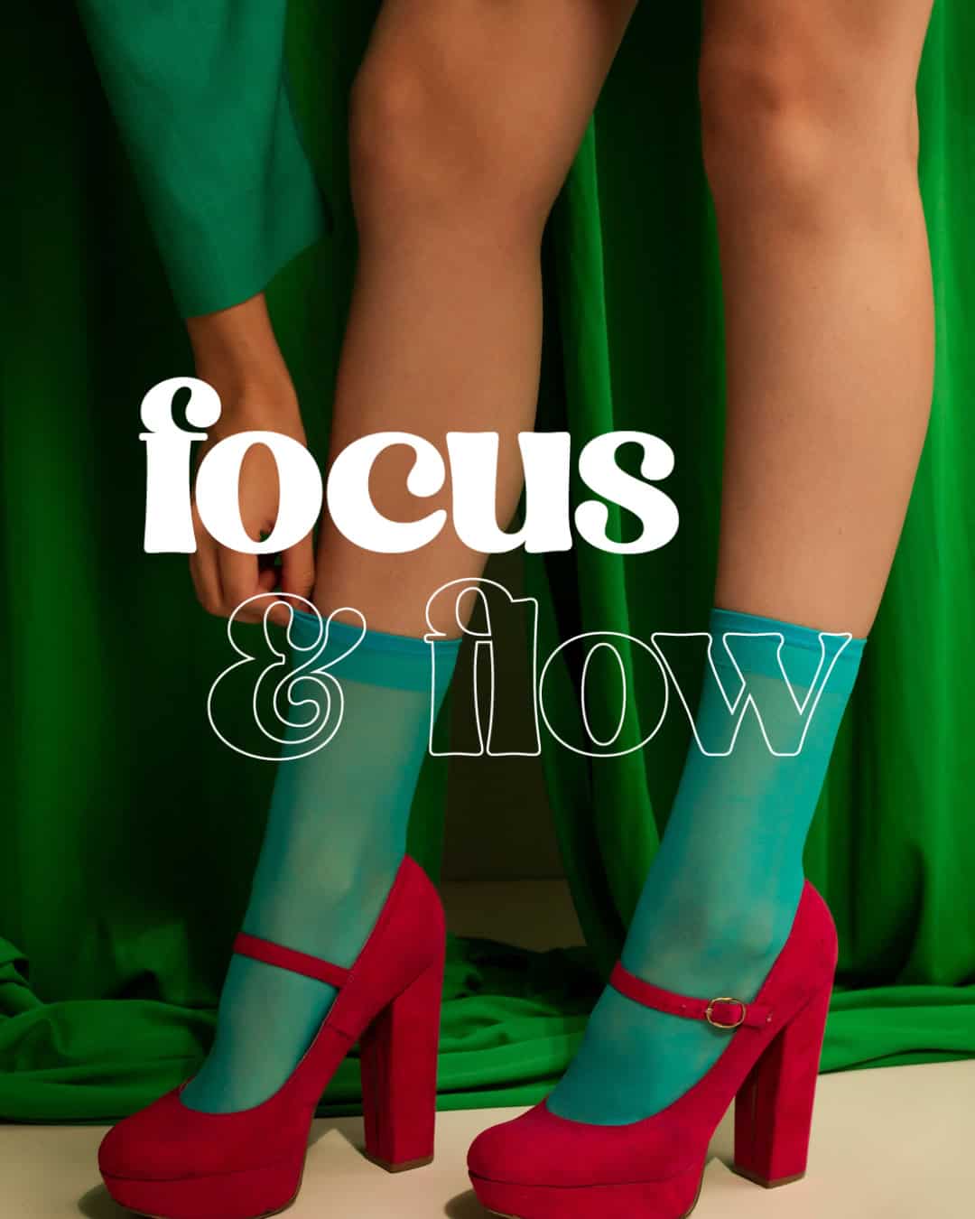 Person wearing bright red high-heeled Mary Jane shoes and translucent blue socks standing against a green fabric backdrop, with the words 'focus & flow' overlaid in white and outlined text.