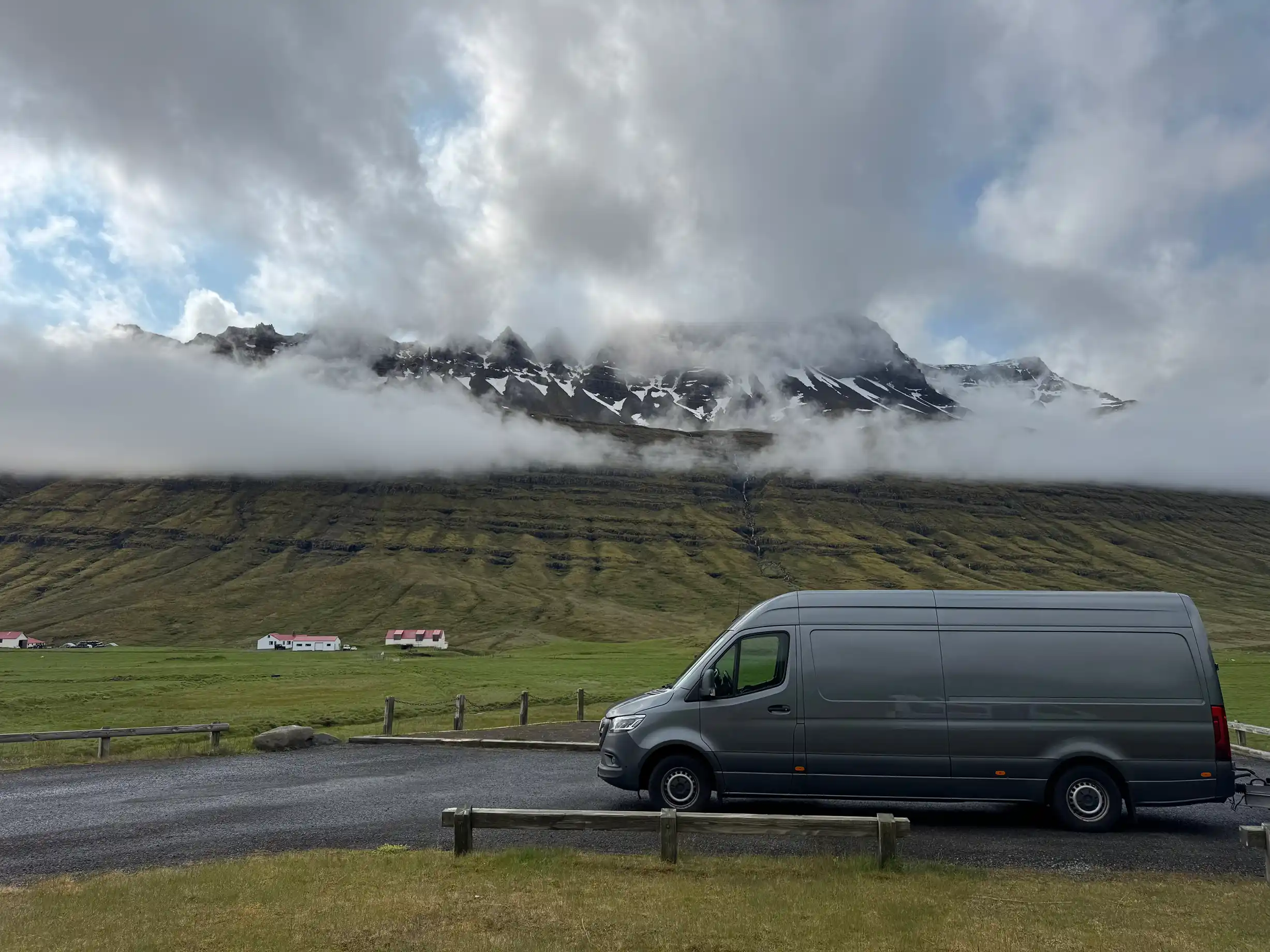 Ein grauer Kleintransporter steht vor einem schneebedeckten, felsigen Berg.